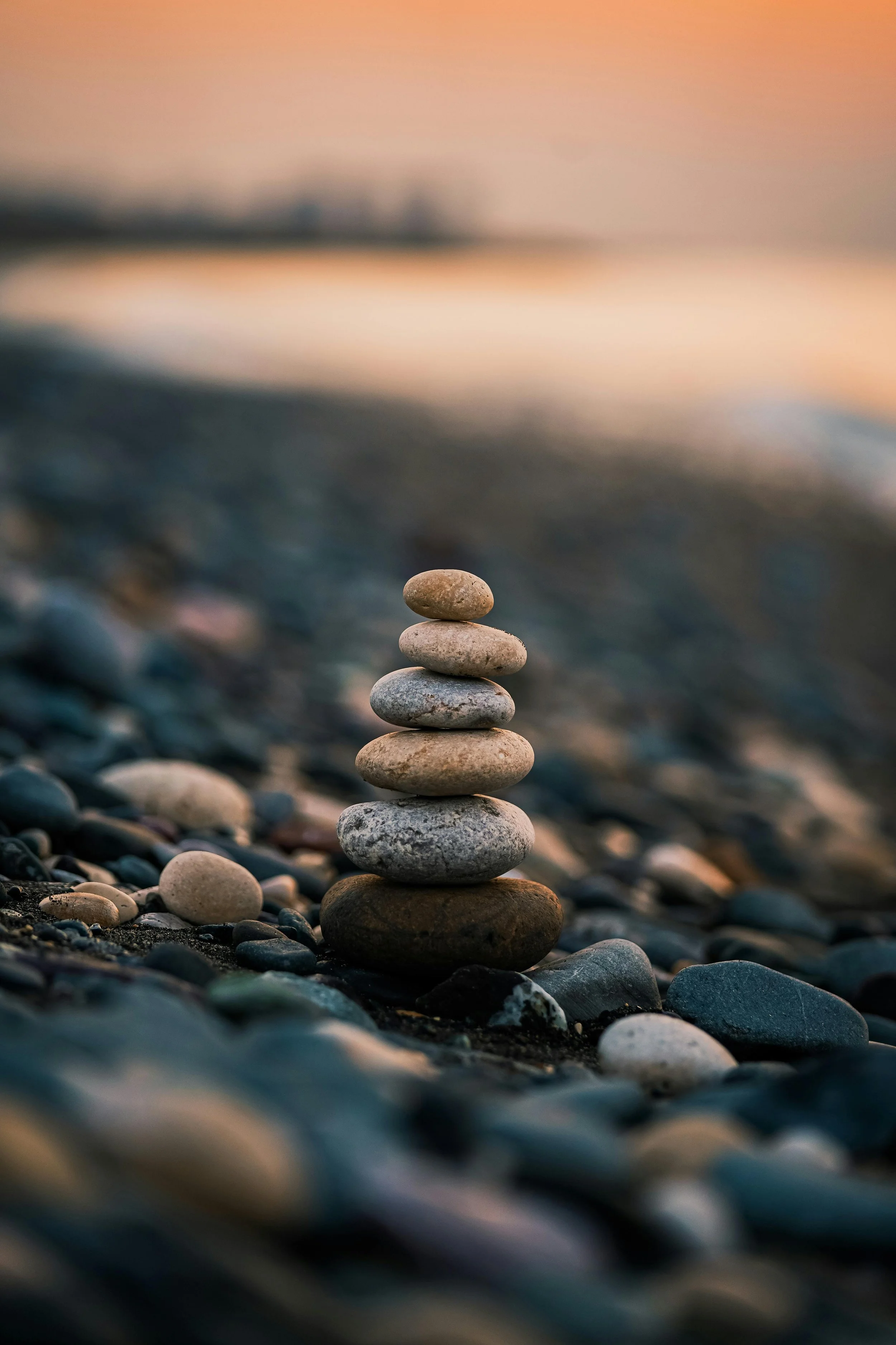 A stack of seven smooth stones balanced on a pebble on a rocky beach during sunset.