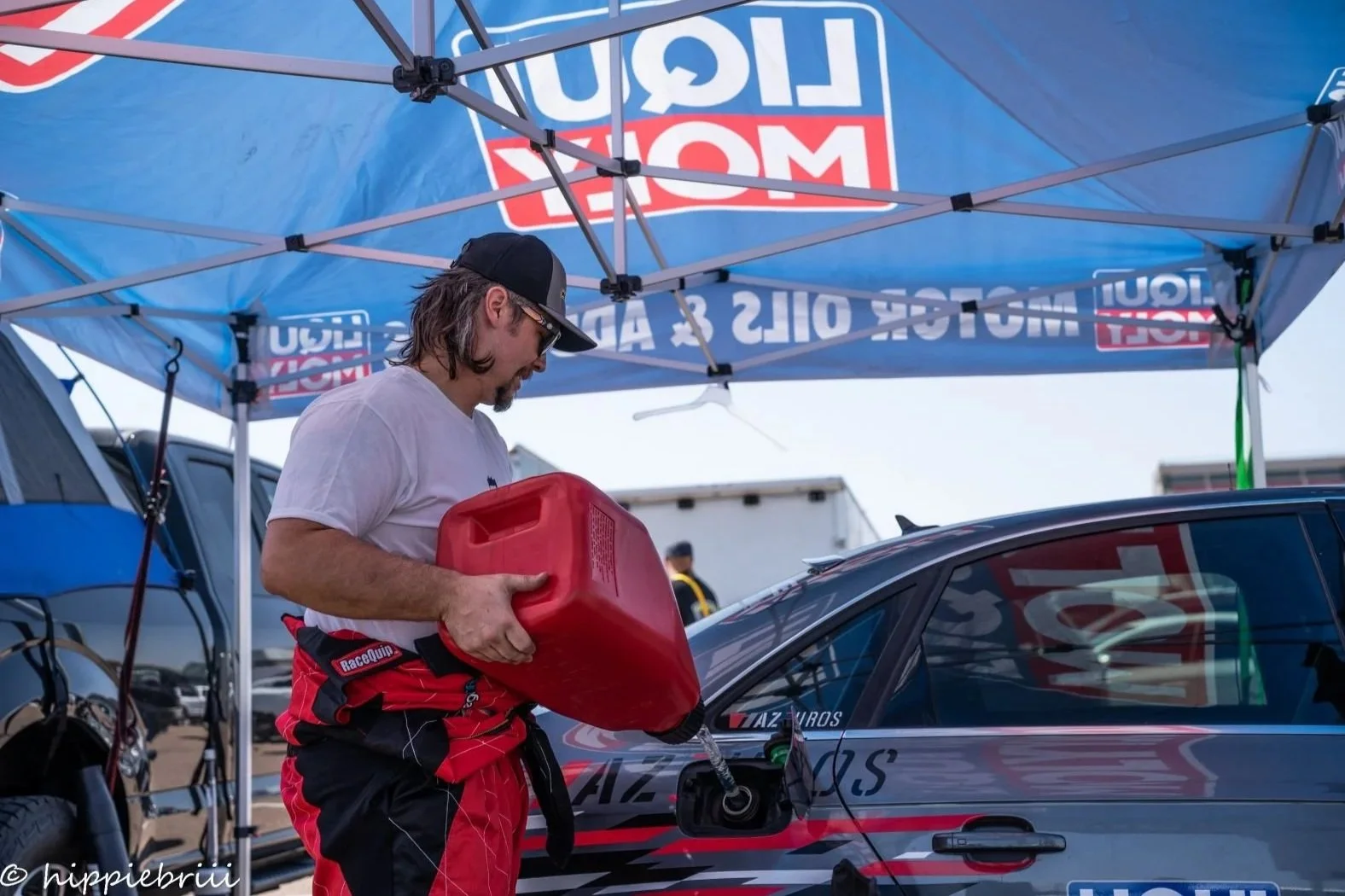 Crew member fueling a performance car under a Liqui Moly canopy in the race paddock, showcasing the Haus of Euro lifestyle.