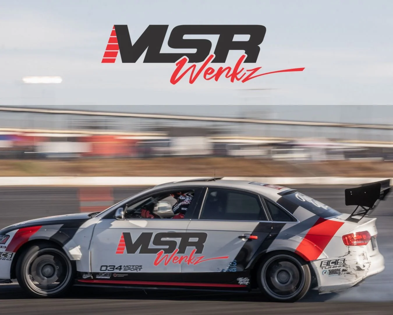 Custom silver Audi drift car wrapped in MSR Werkz livery drifting sideways on a track during a performance driving event.