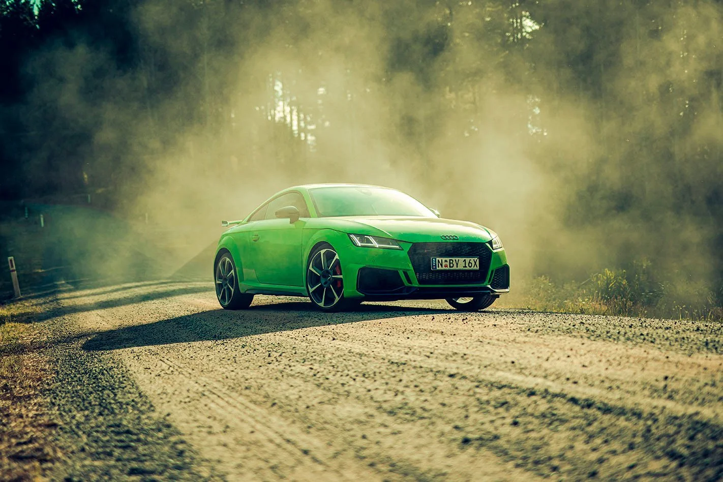 A bright green Audi sports car parked on a gravel road amidst a foggy, wooded area during daylight.