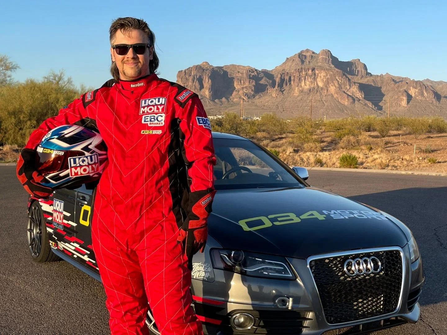 Austin Phipps of MulletSport Racing smiling trackside next to the custom fire-liveried Audi performance build supported by Haus of Euro.