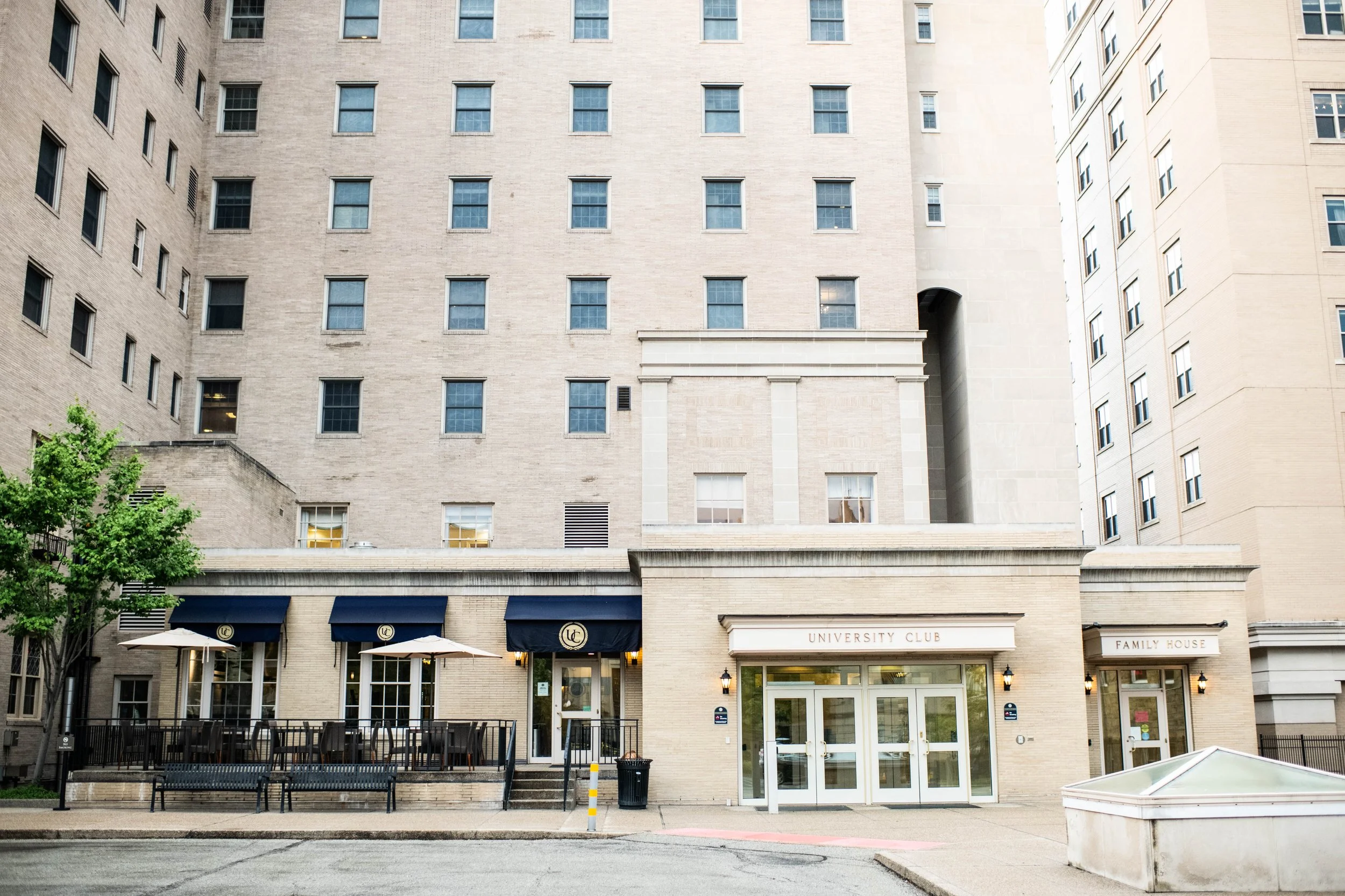 University Club and the University of Pittsburgh | Exterior view of a city building with a restaurant patio area and signs reading 'University Club' and 'Family House'.