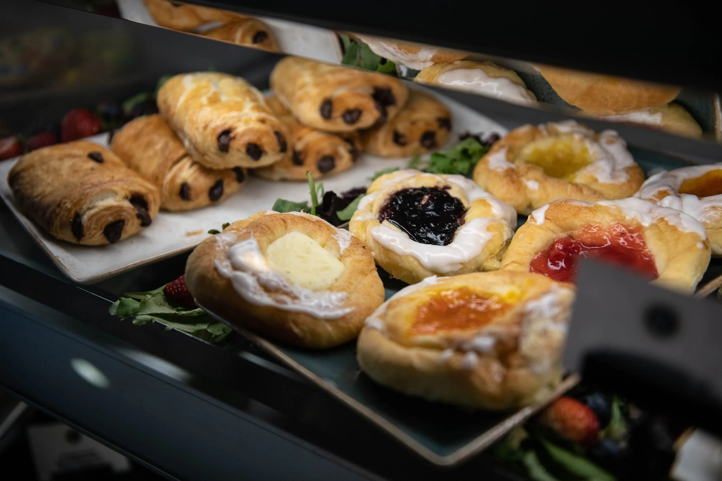 Assorted baked goods including Danish pastries with various fruit and cream fillings displayed on trays.