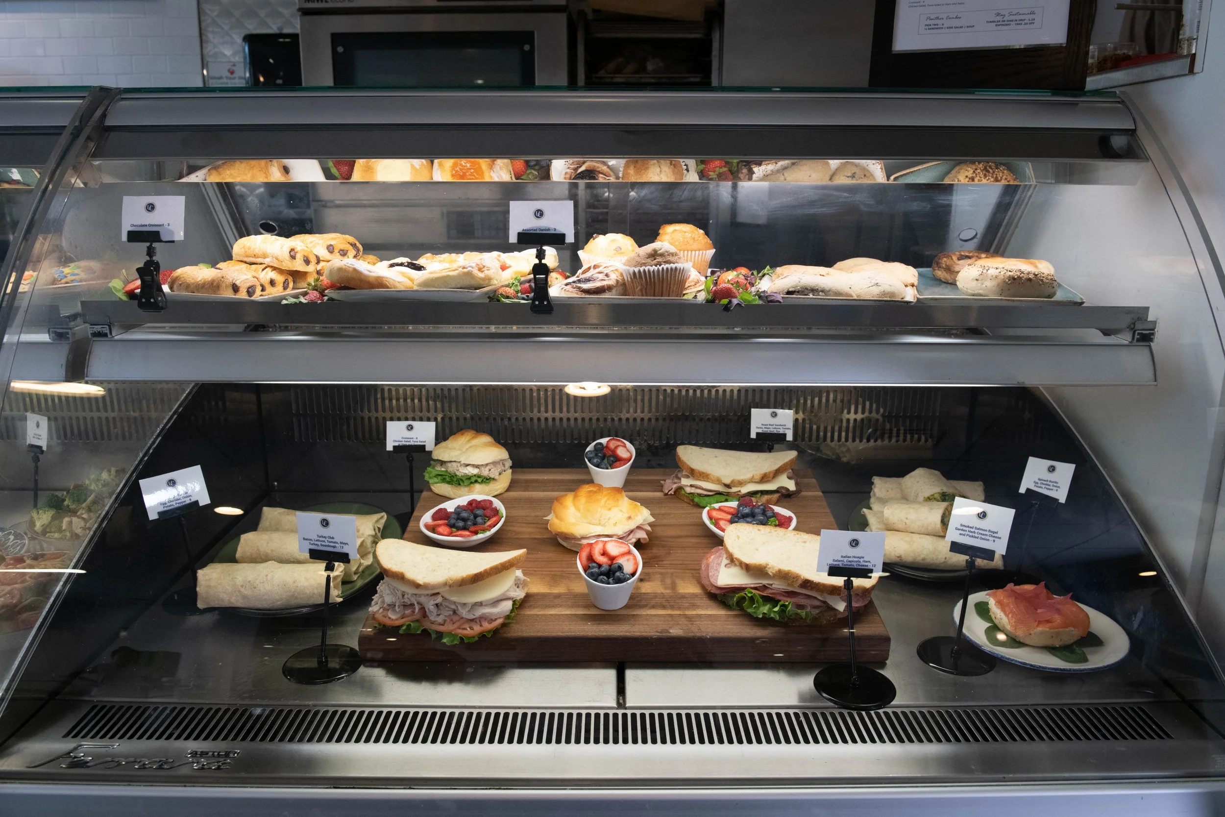 Cafe 1923 at University Club | A display case with various pastries and sandwiches, including muffins, scones, and bagels on the top shelf, and different sandwiches. Open to public Monday-Friday.