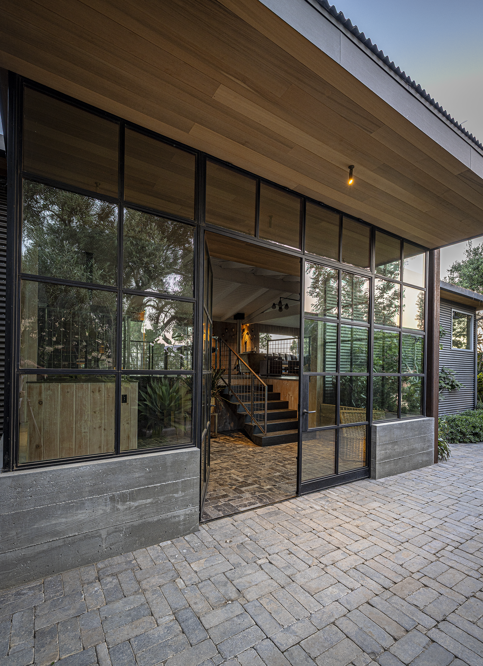 Exterior view of a modern building with large glass windows, a gravel pathway, and trees visible through the windows.