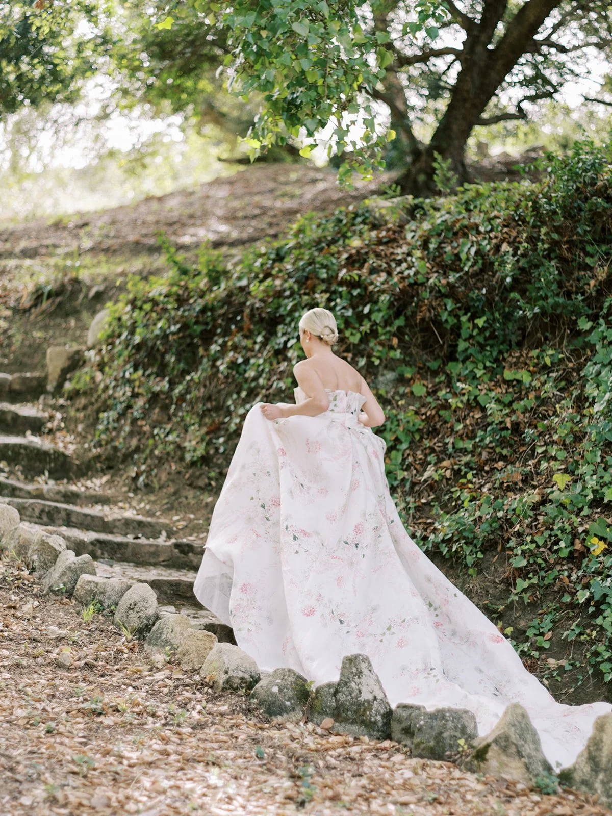 Woman in floral gown walking up stone steps in a wooded area in Portugal