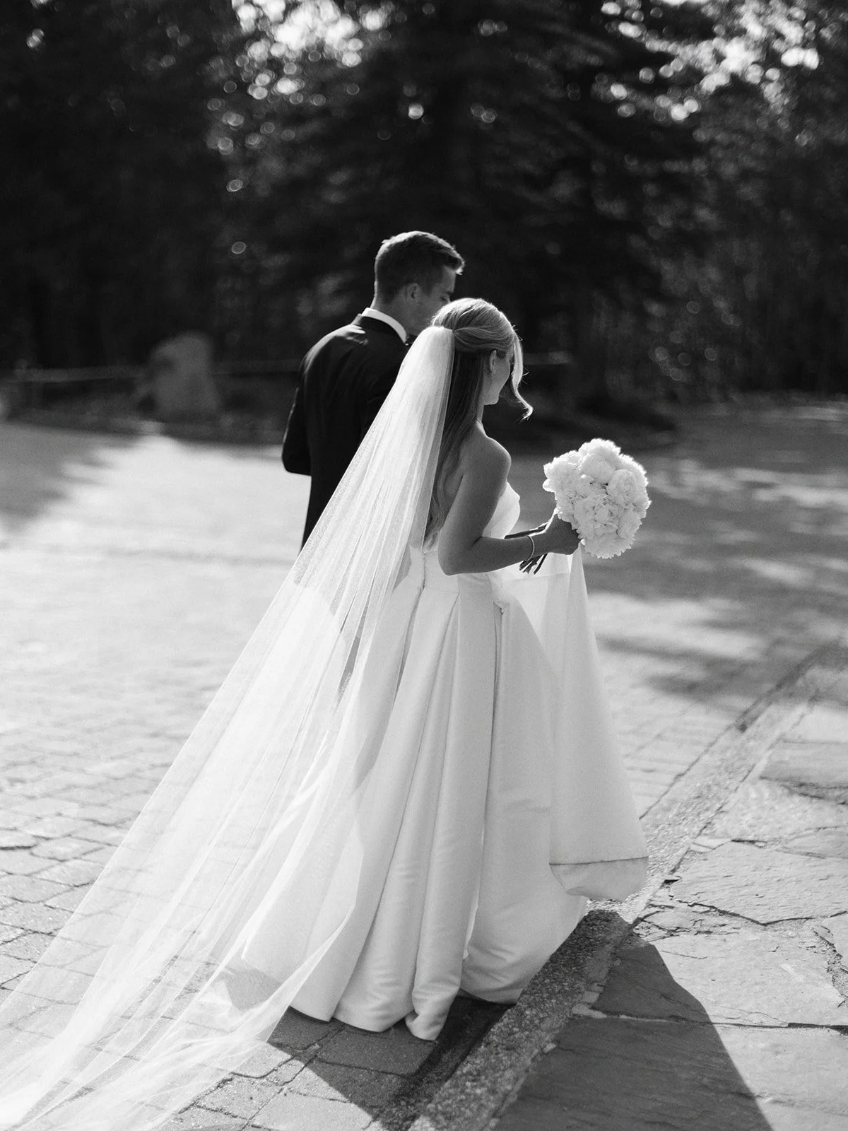 Bride and groom walking outdoors, bride holding a bouquet, monochrome image.