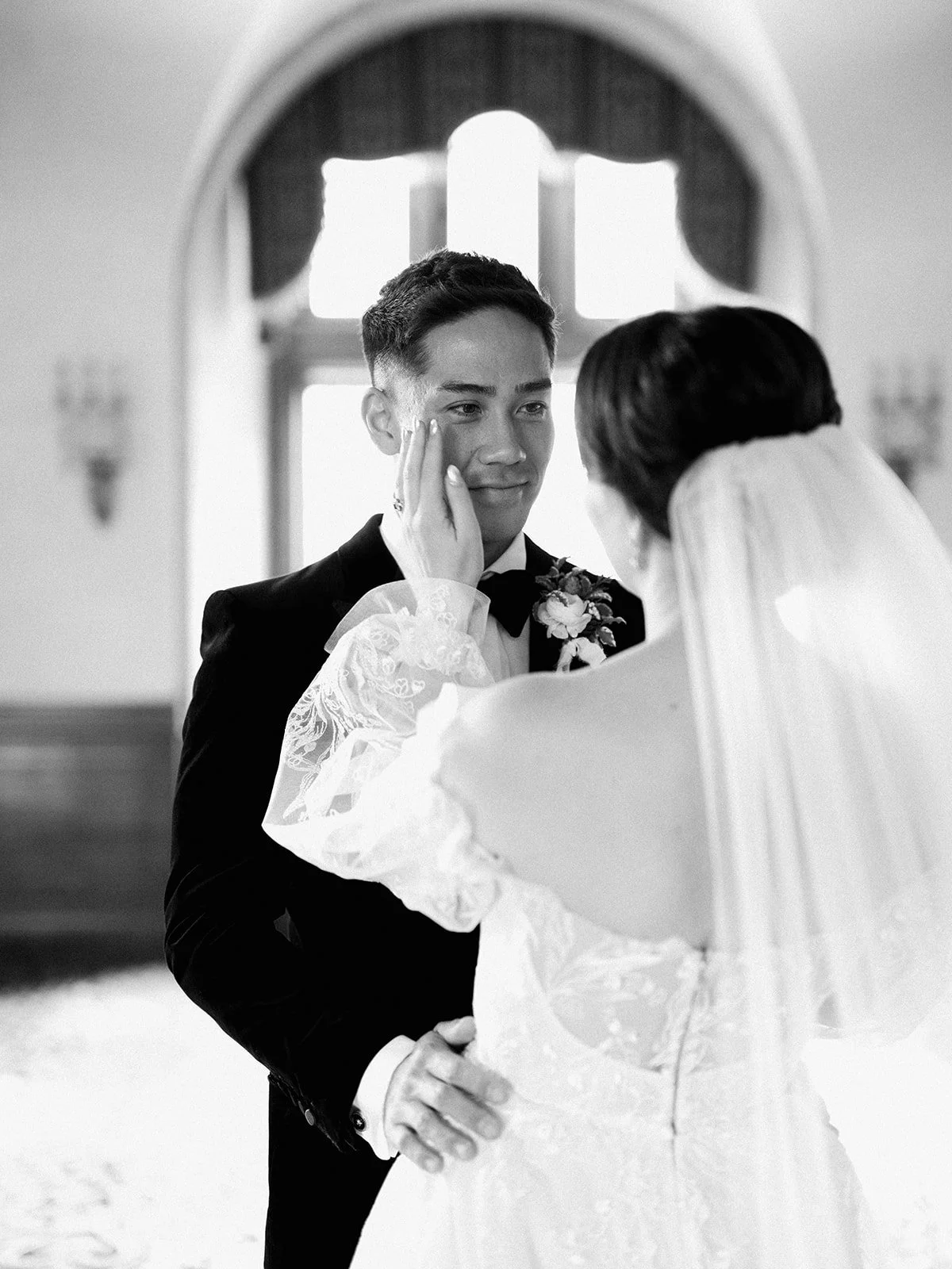 Bride and groom sharing a tender moment, with the bride touching the groom's cheek, in a bright room.
