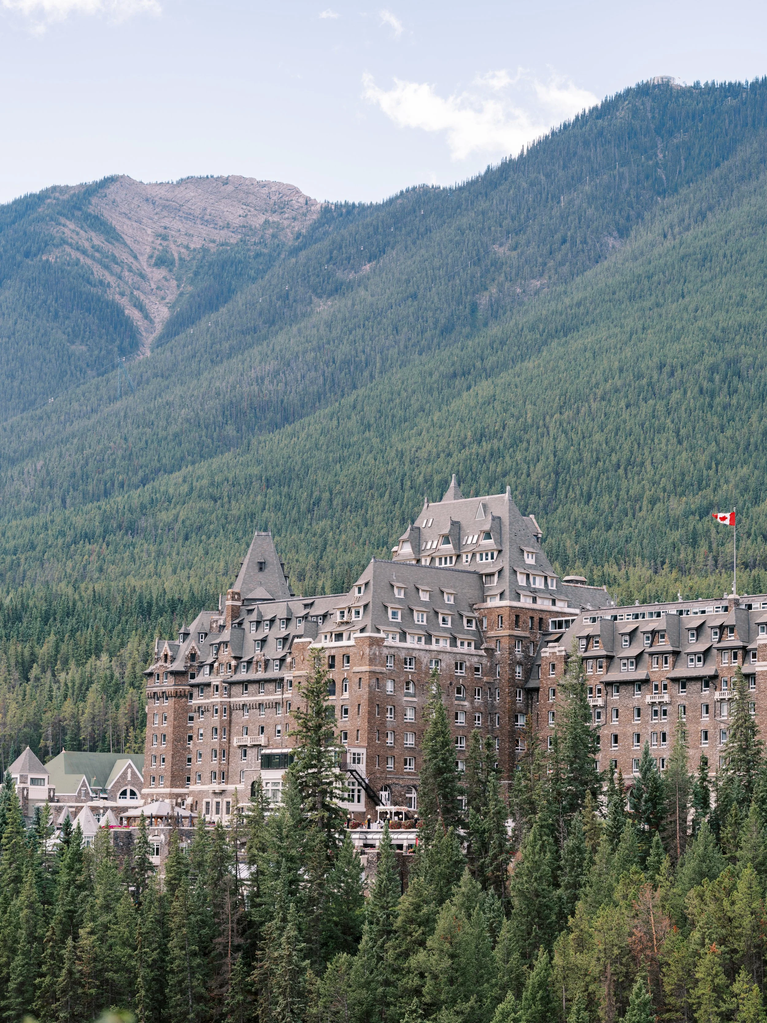 Large historic hotel nestled in a forested mountain landscape. The Fairmont Banff Springs Hotel