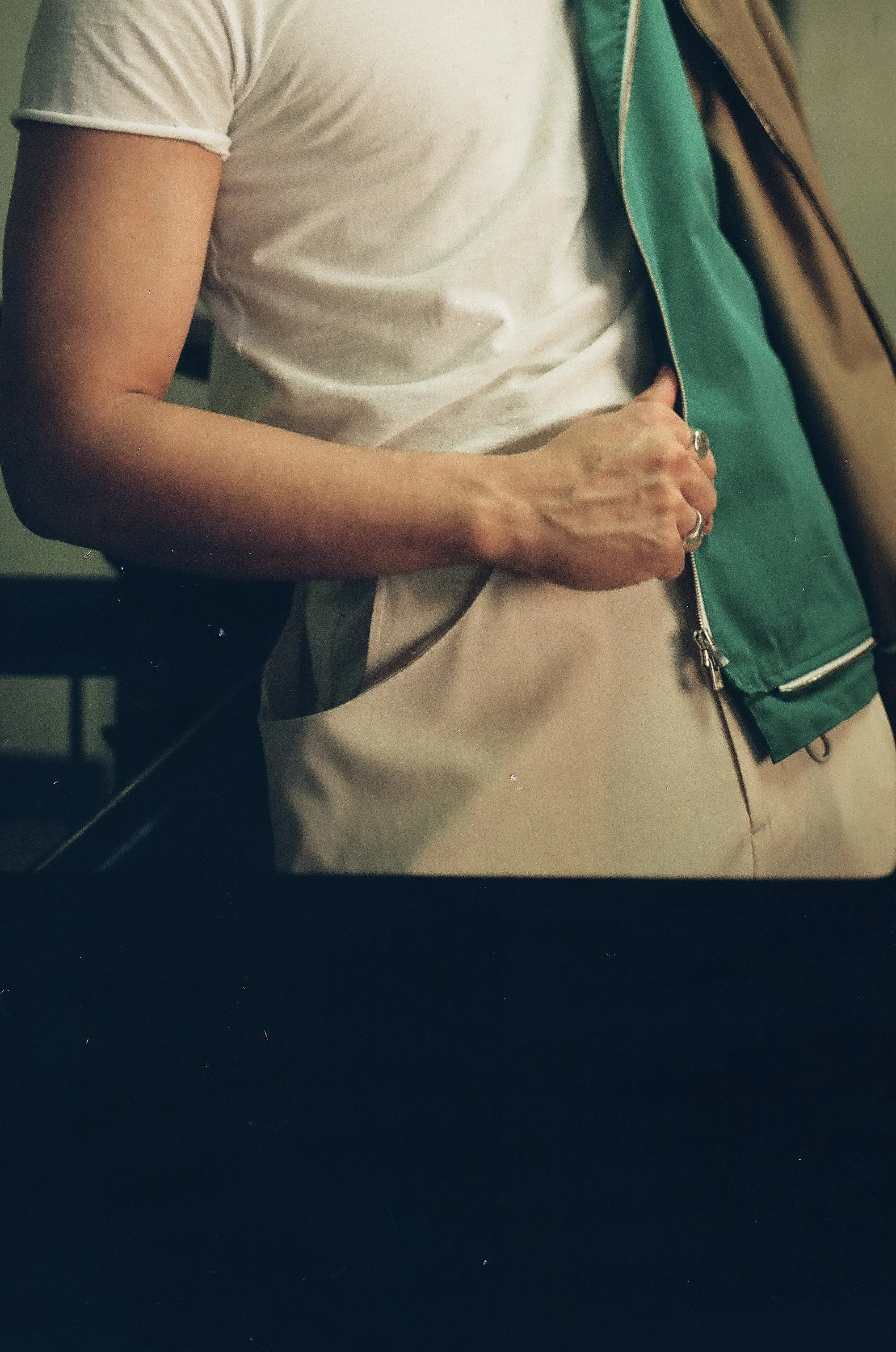 Person wearing a white t-shirt and beige pants, holding open a green and brown jacket.