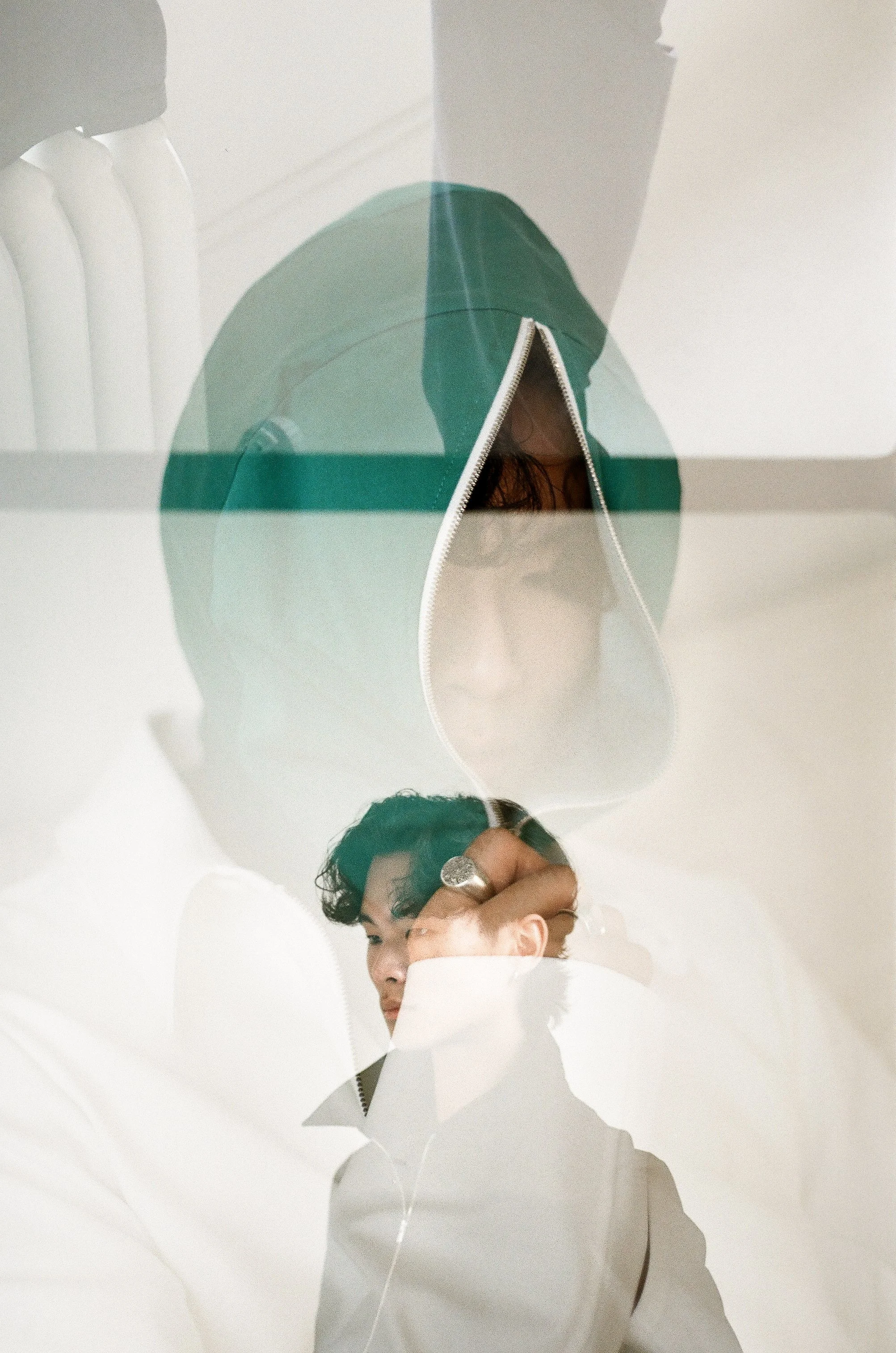 A double exposure photo of a woman with glasses, wearing a hooded jacket, and a man adjusting his collar, seen through a glass surface.