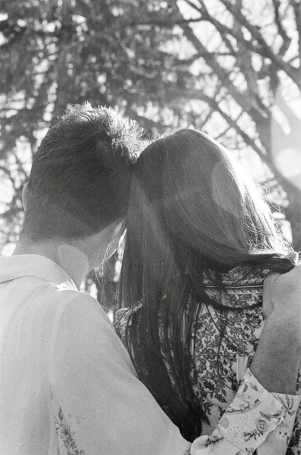 A black and white photograph of a couple with their faces close together, under trees.