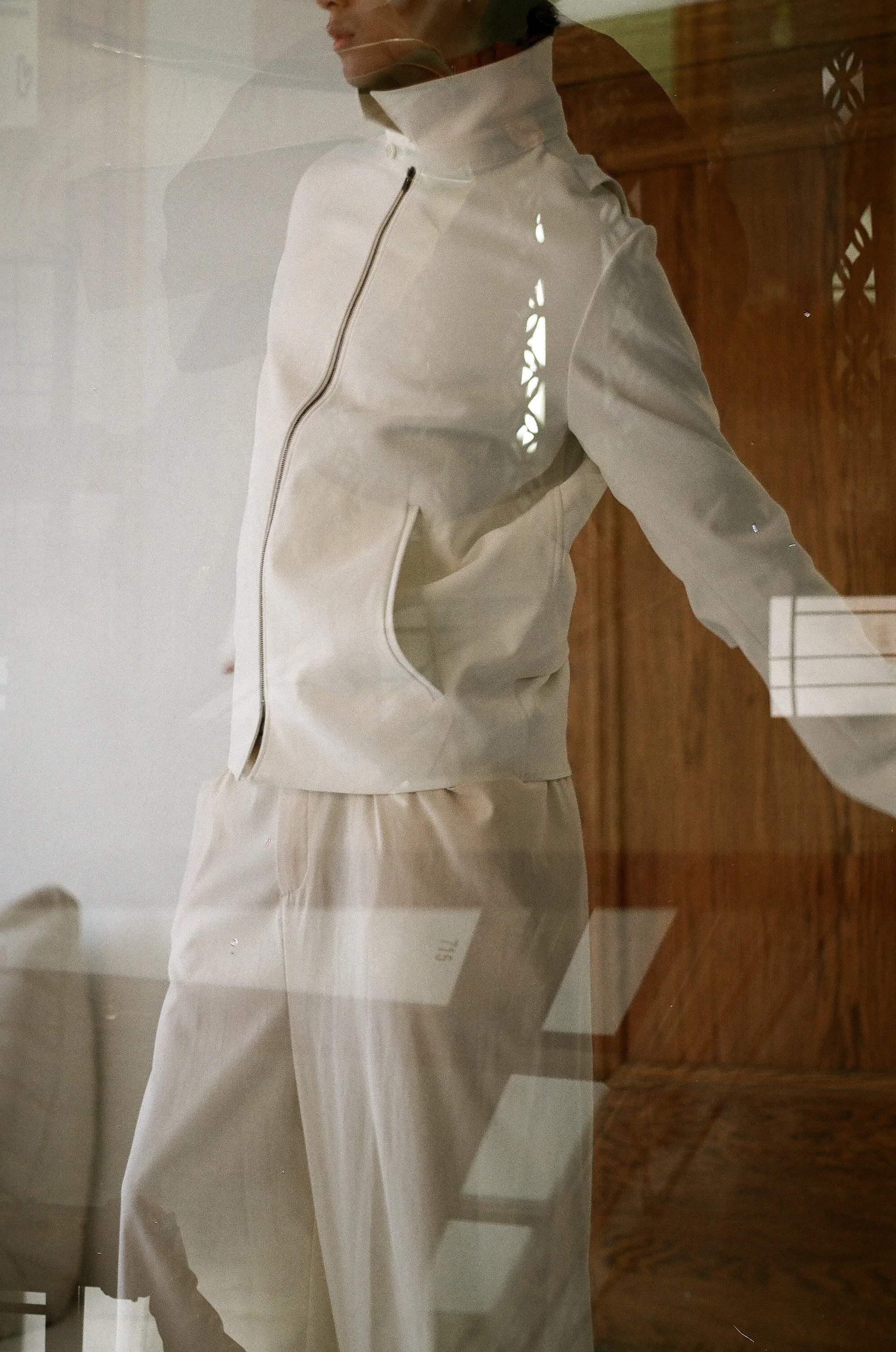 Person wearing an off-white zip-up jacket and matching pants, reflected in a glass display case.
