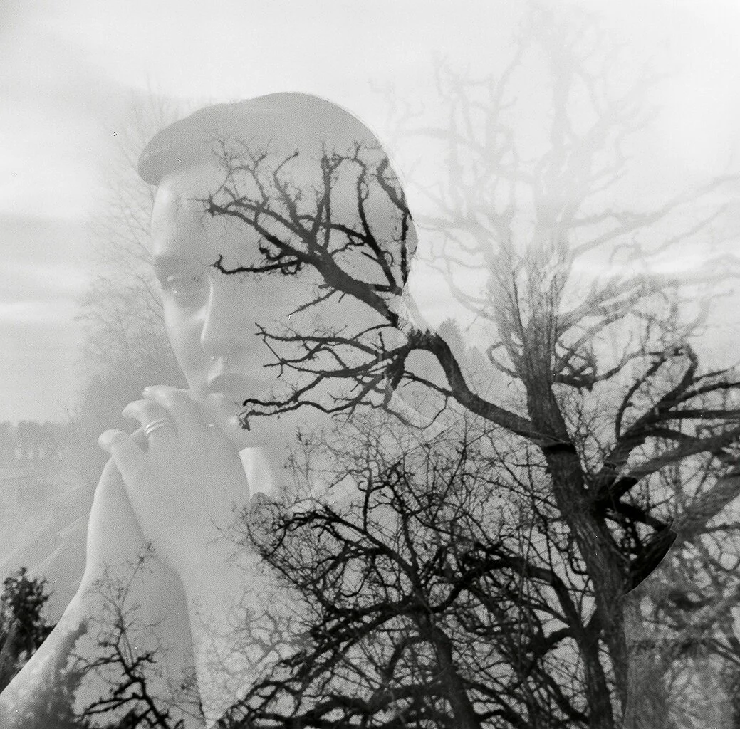 A double exposure photo blending a woman's profile with a leafless tree against the sky.