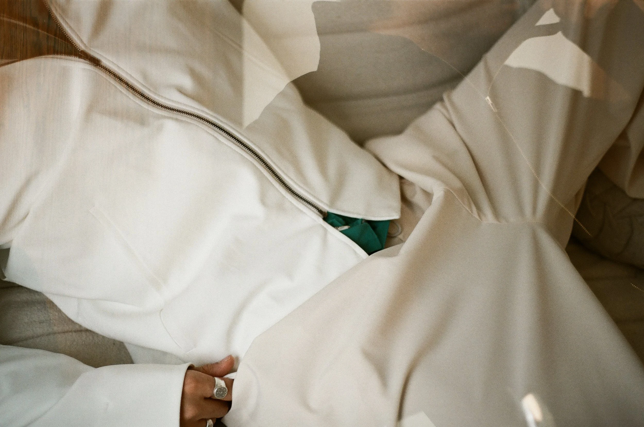 Close-up of a person wearing a white jacket with a zipper, their hand with a ring visible, partially tucked into the jacket.