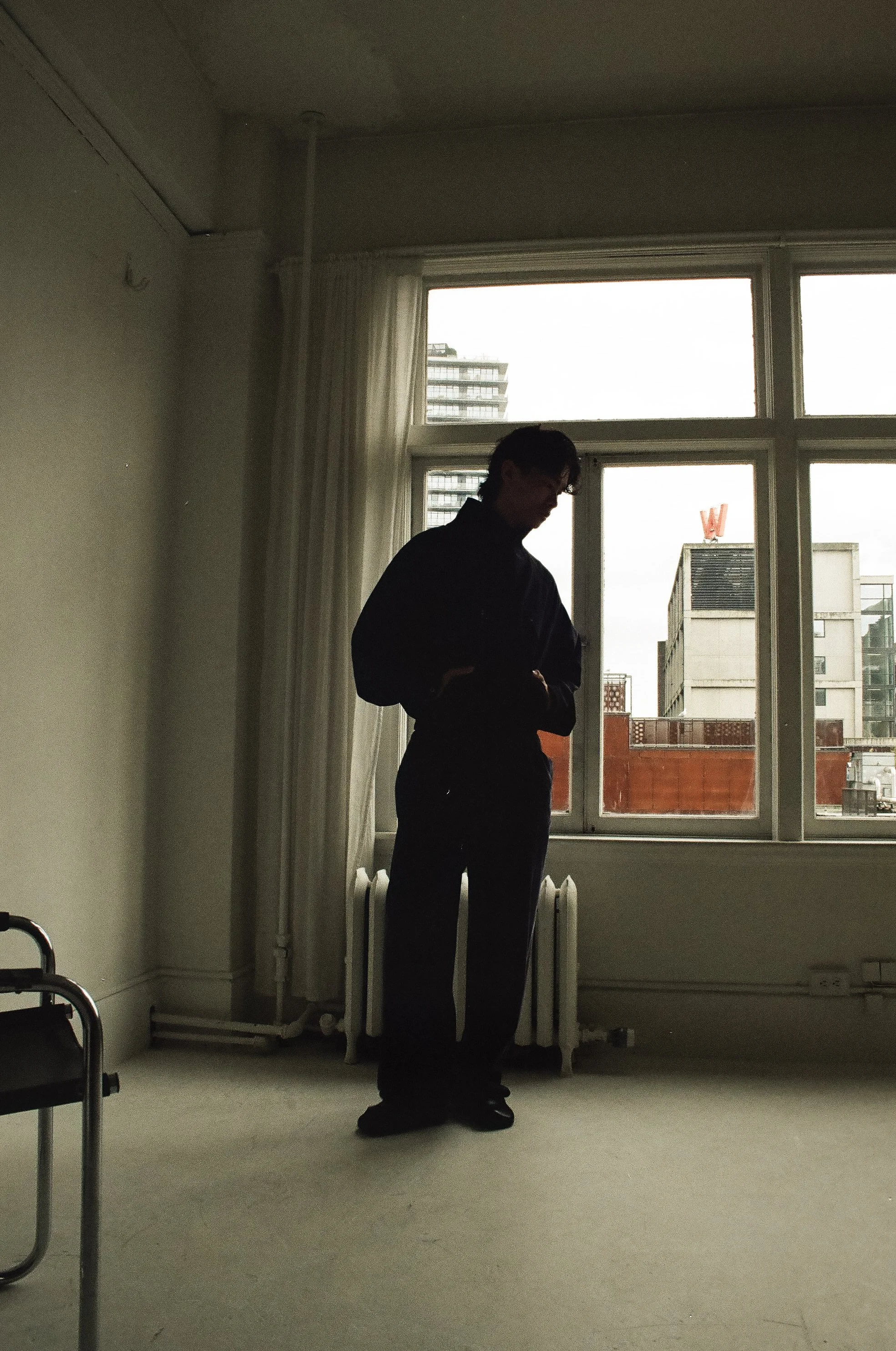 Silhouette of a person standing indoors near a large window with city buildings visible outside.