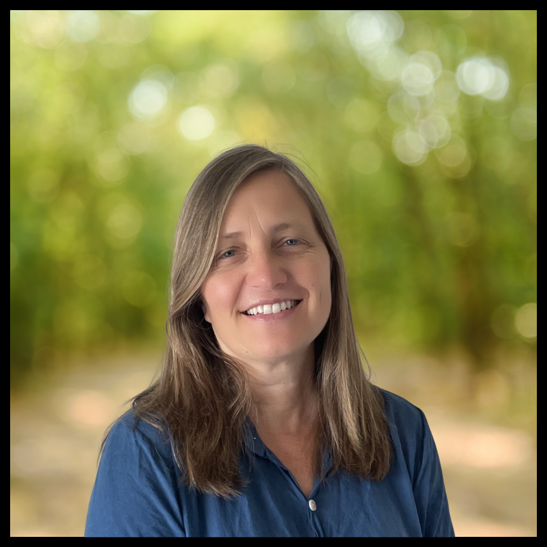 A woman wearing a blue shirt stands against a blurred background.