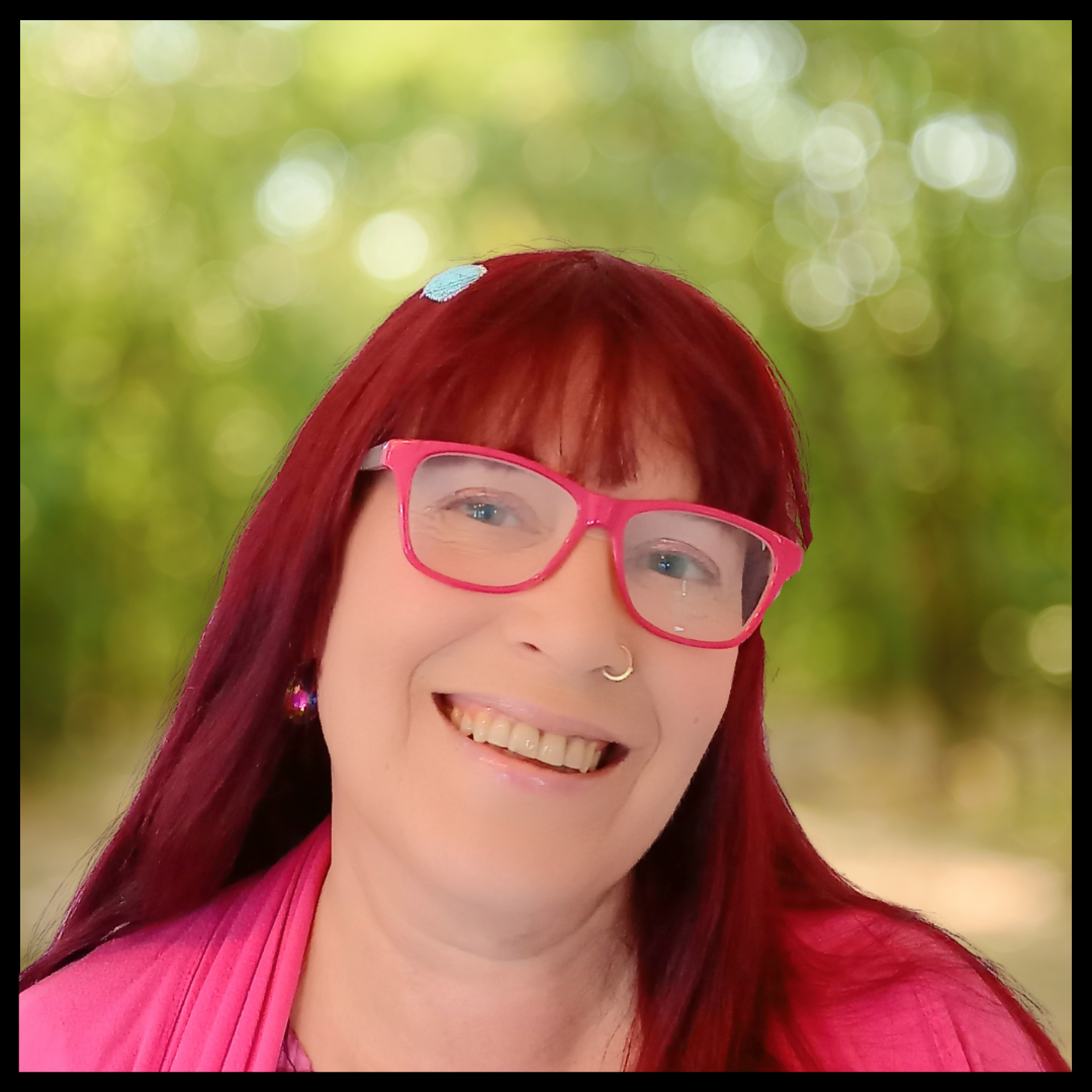 A woman with long striking red hair and smiling, wearing stylish glasses, against a softly blurred background.