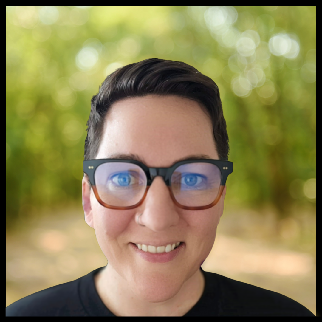 A person with short dark hair, wearing thick glasses and smiling.