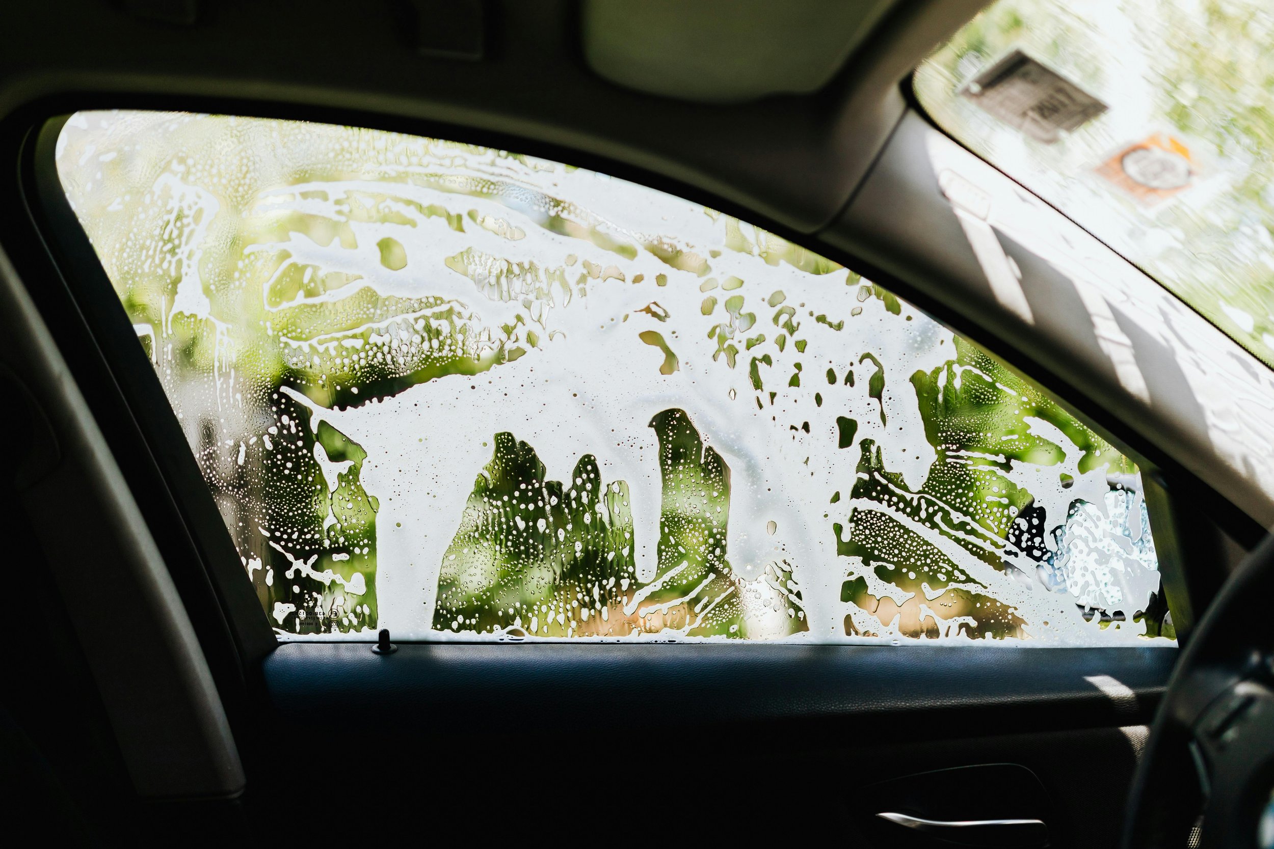 Car interior with the windshield covered in soap suds and cleaning foam.