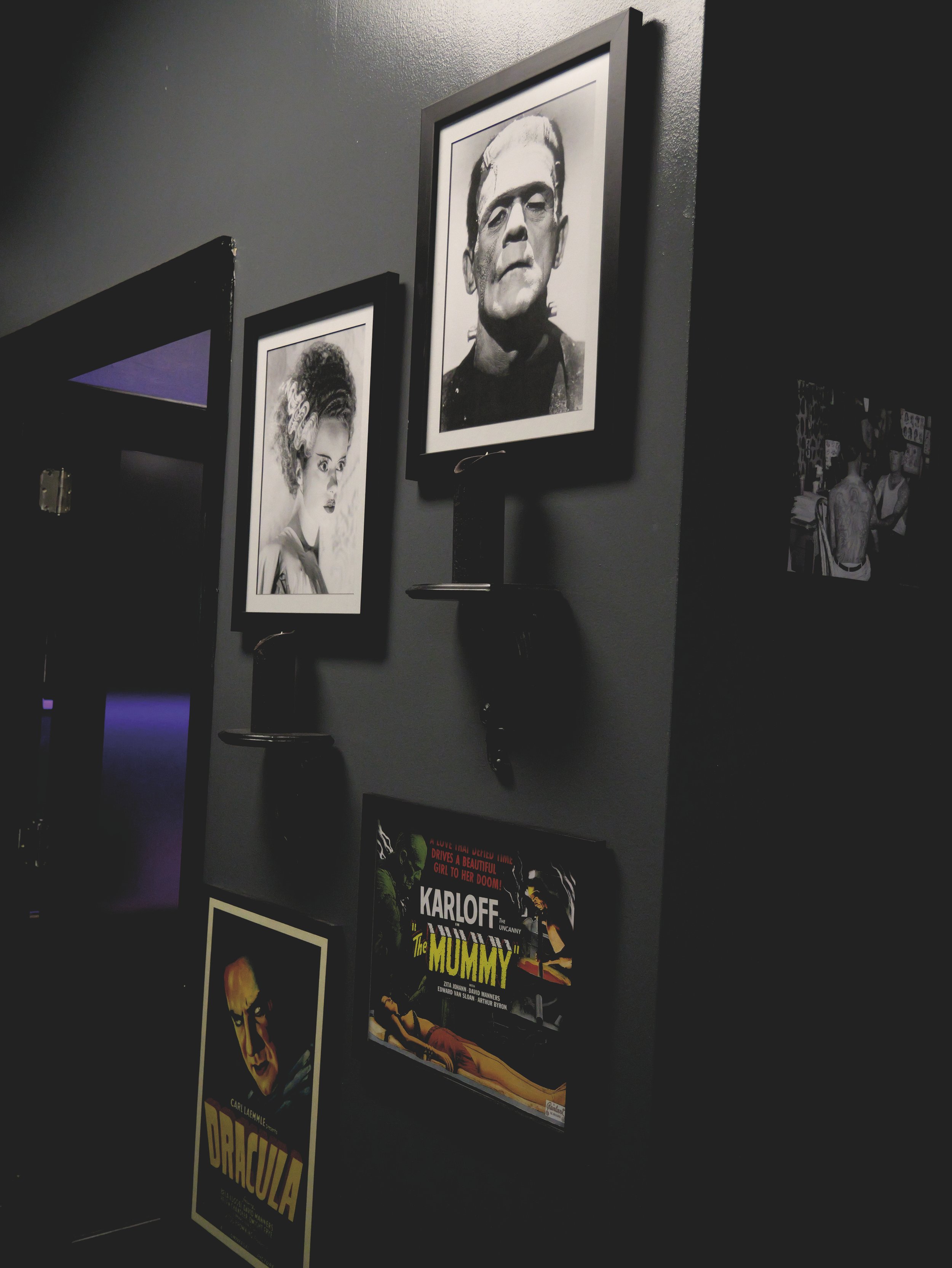 Wall with framed black and white photos of classic movie monsters, including Frankenstein's monster and the Bride of Frankenstein, alongside vintage posters for "Dracula" and "The Mummy."