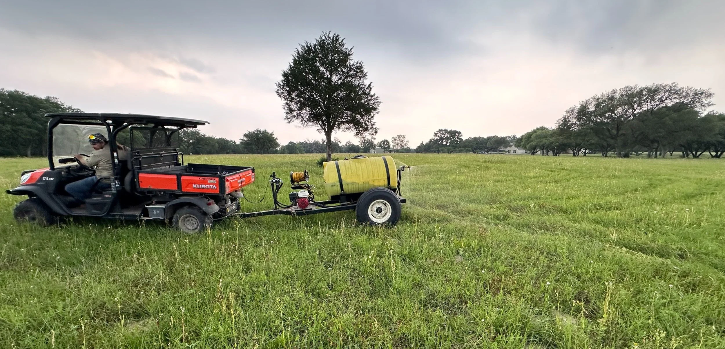 Small work truck spraying liquid compost extract in a large field.