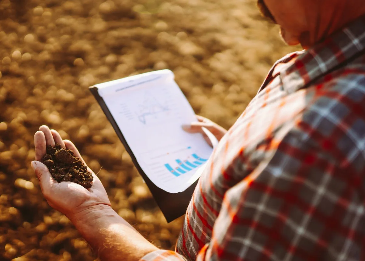 Farmer holding clipboard with observing a handful of dirt.