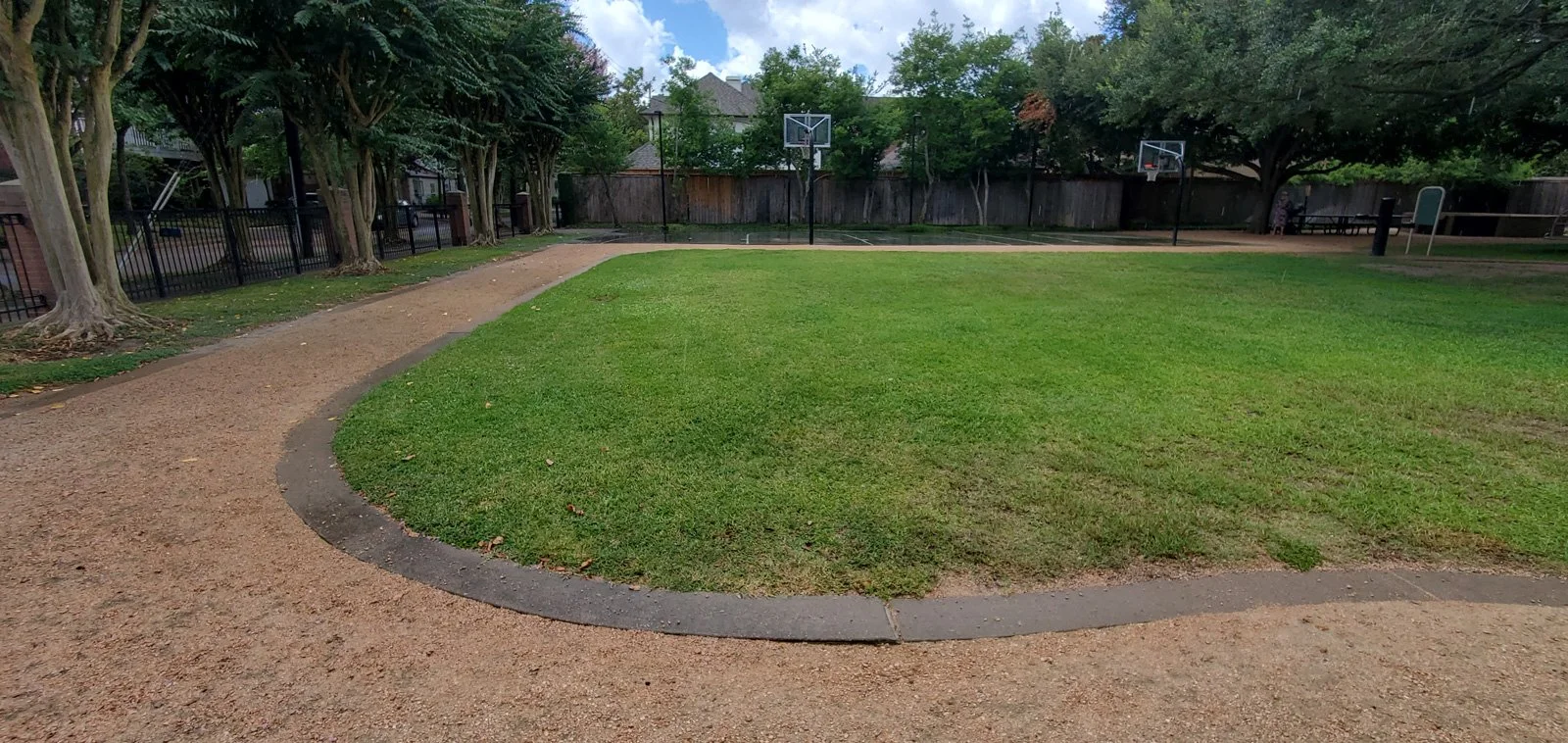 Small park with basketball hoops, walking trail, and large grassy area.