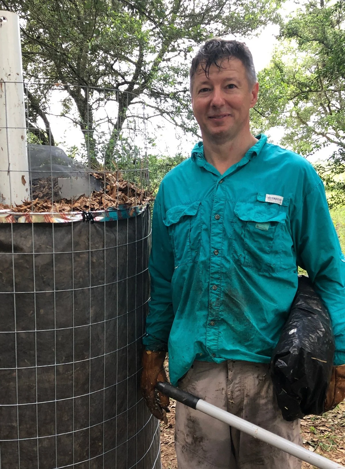 Alistair wearing a teal shirt standing outside under some trees.