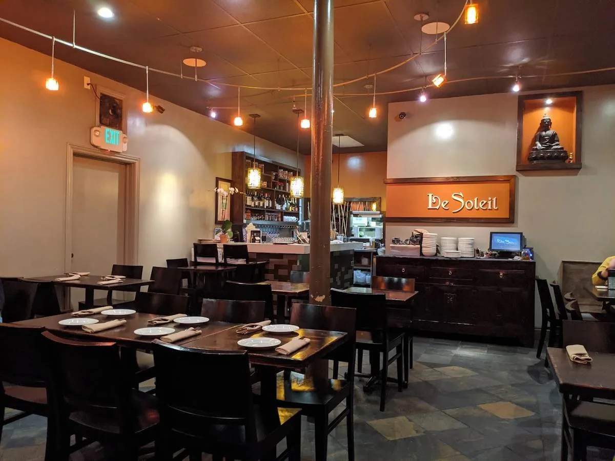 The dining room at Le Soleil on Clement Street — dark wood tables beneath warm pendant lights, with the bar at the back