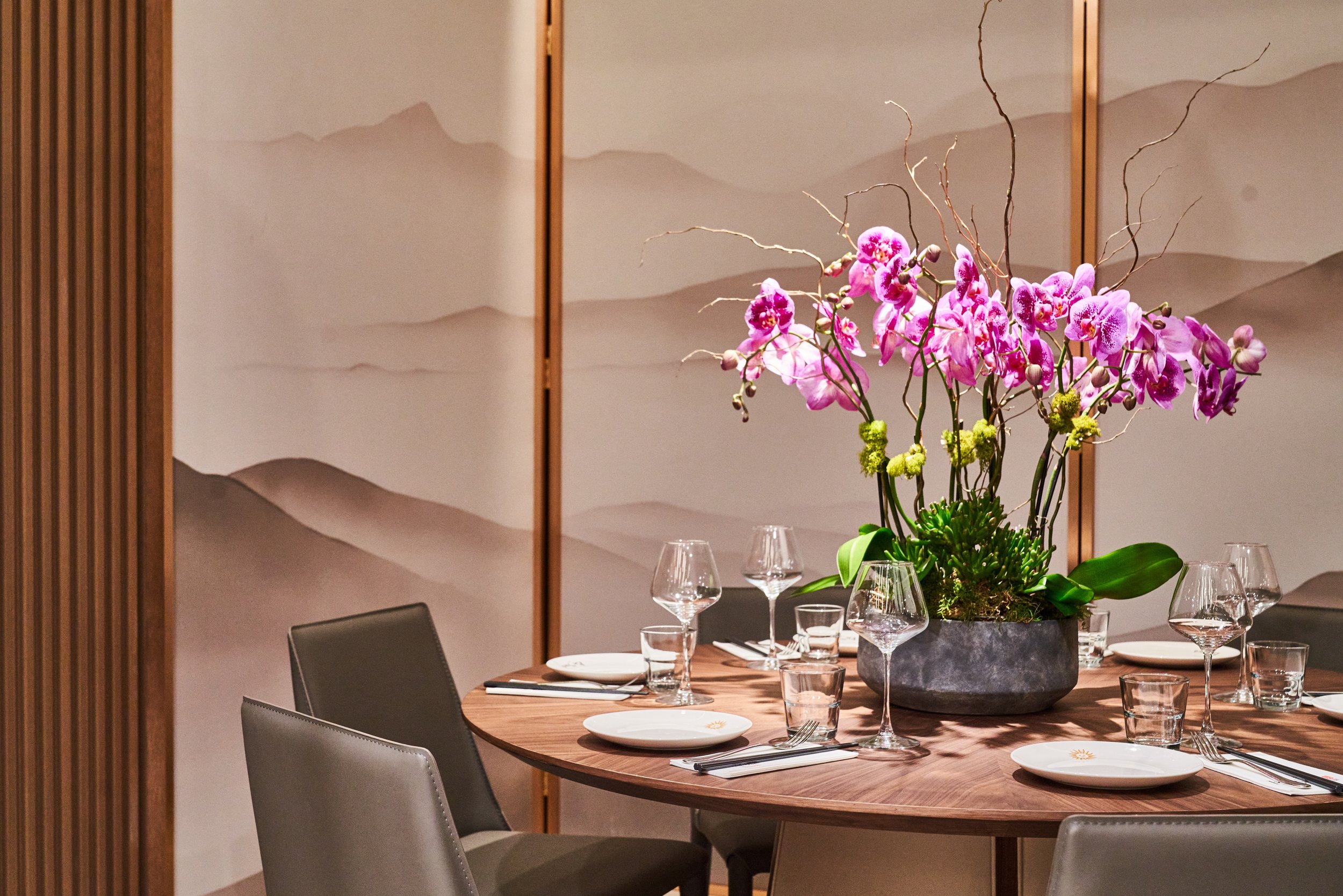 The private room at Le Soleil Stonestown — a round table set with orchids before a painted mountain screen