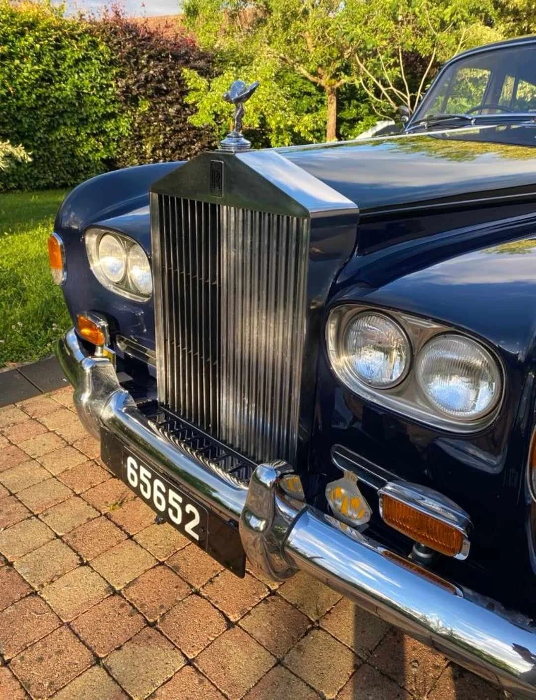 Une voiture ancienne de couleur bleue avec un pare-chocs en chrome, un radiateur vertical emblématique et un emblème de l'esprit de la voiture sur le capot.
