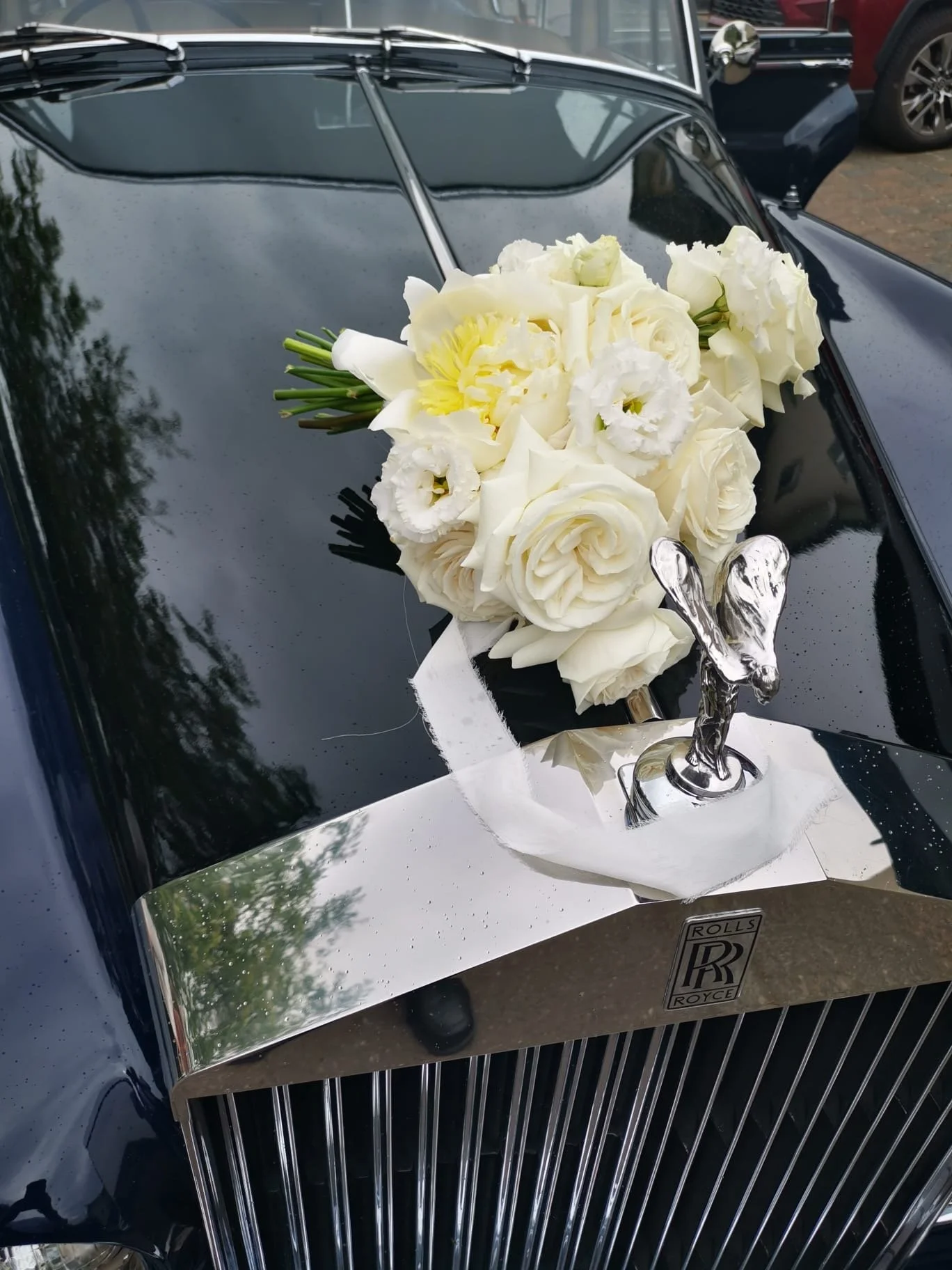 Une bouquet de fleurs blanches posé sur la calandre d'une voiture Rolls-Royce noire.