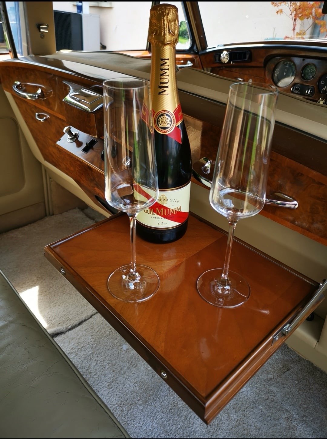 Une bouteille de champagne et deux flûtes à champagne sur une petite table en bois dans l'intérieur d'une voiture de luxe en bois.