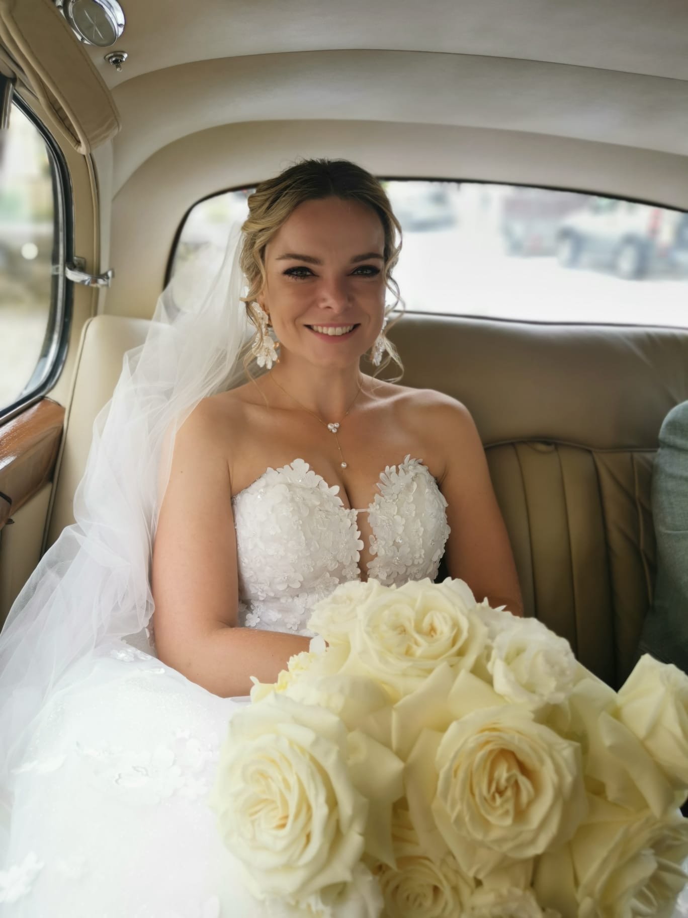 Jeune femme en robe de mariage avec bouquet de roses blanches dans une voiture