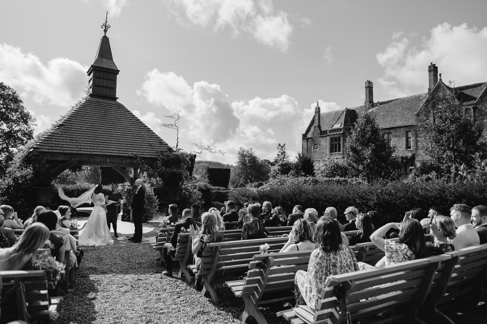 wide shot of groom and bride at front of outdoor ceremony, brides veil being blown by the wind