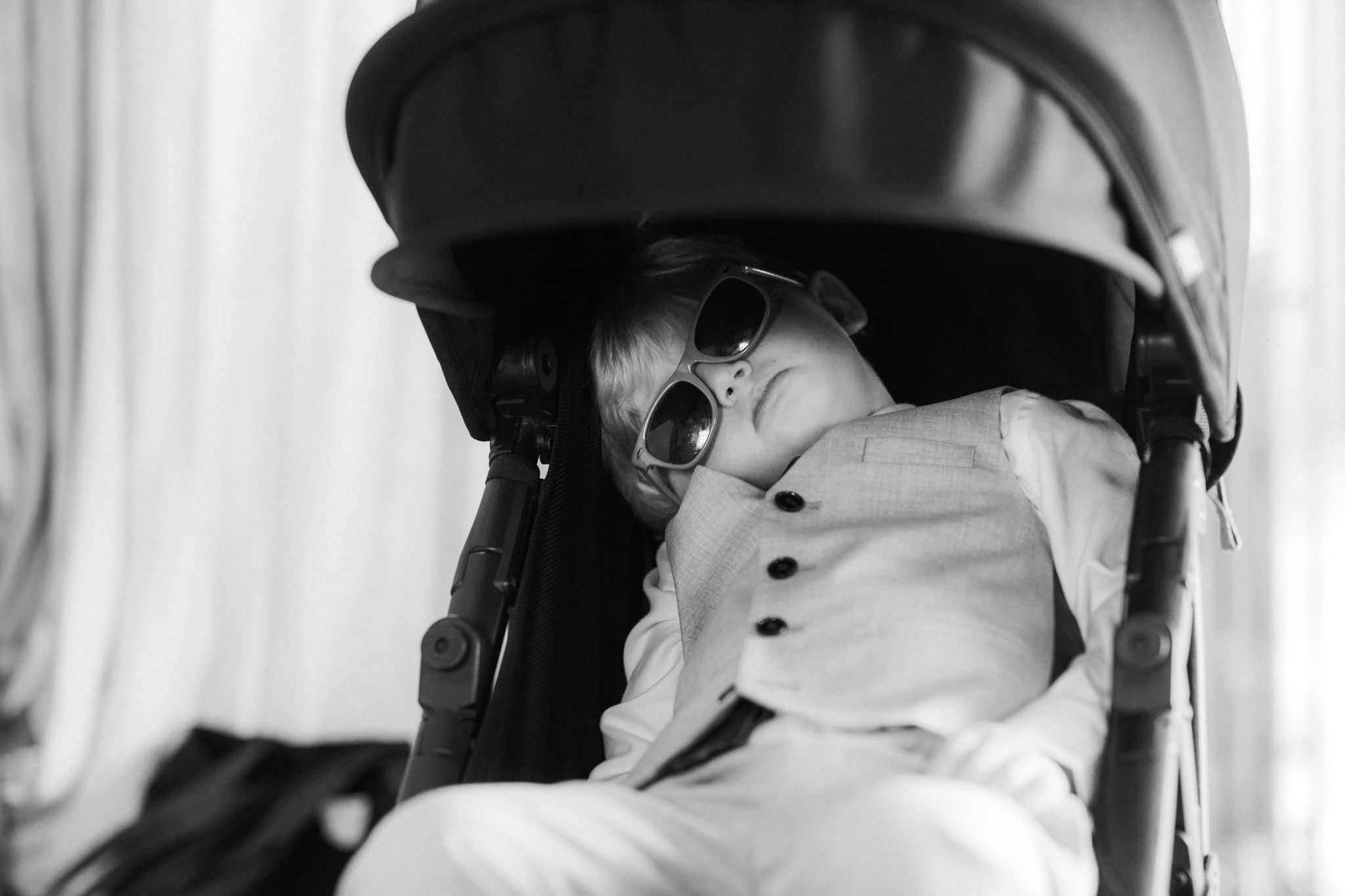 candid photo of little boy asleep in pram wearing sunglasses
