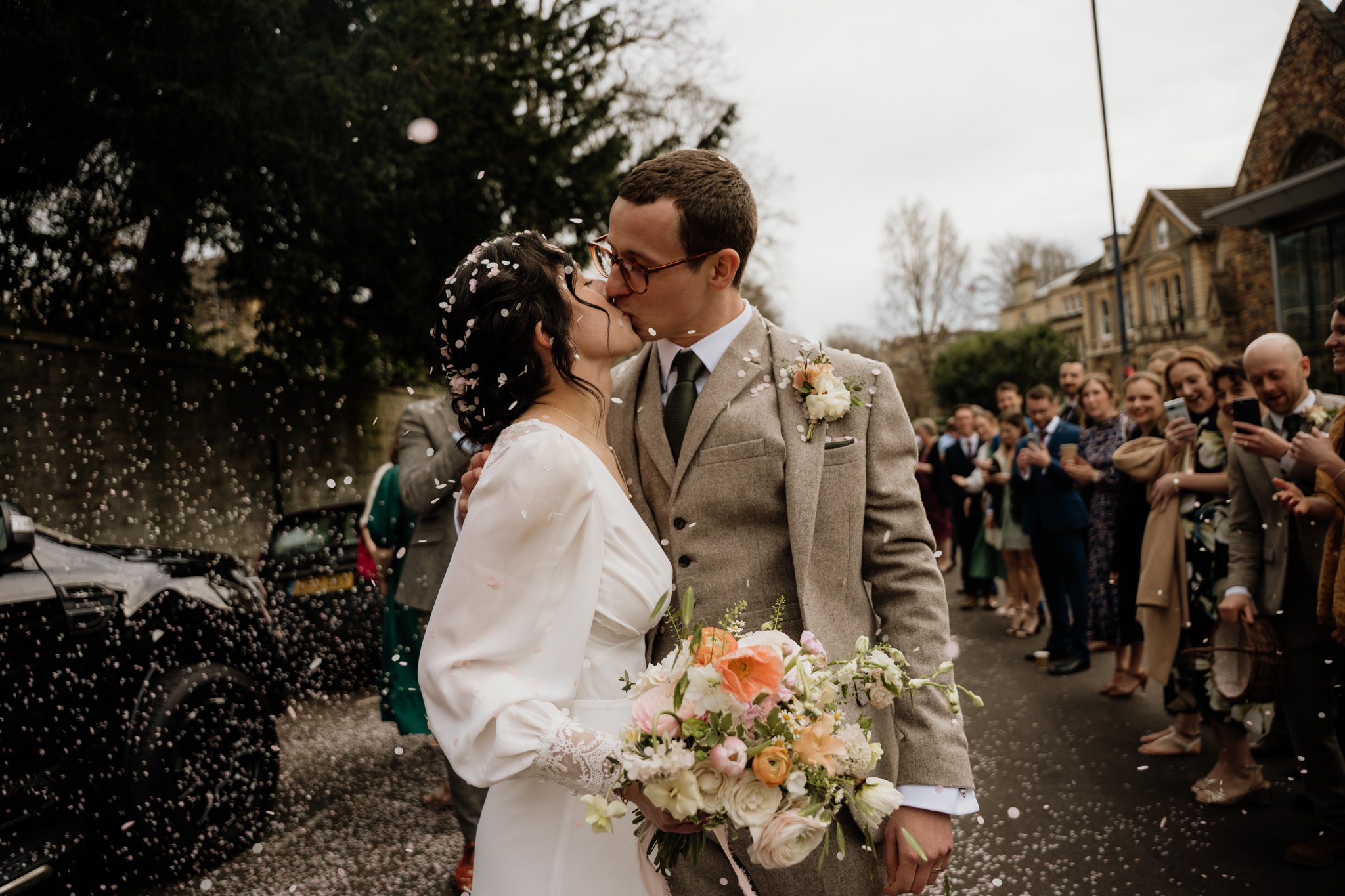 bride and groom kiss during confetti tunnel on bristol street