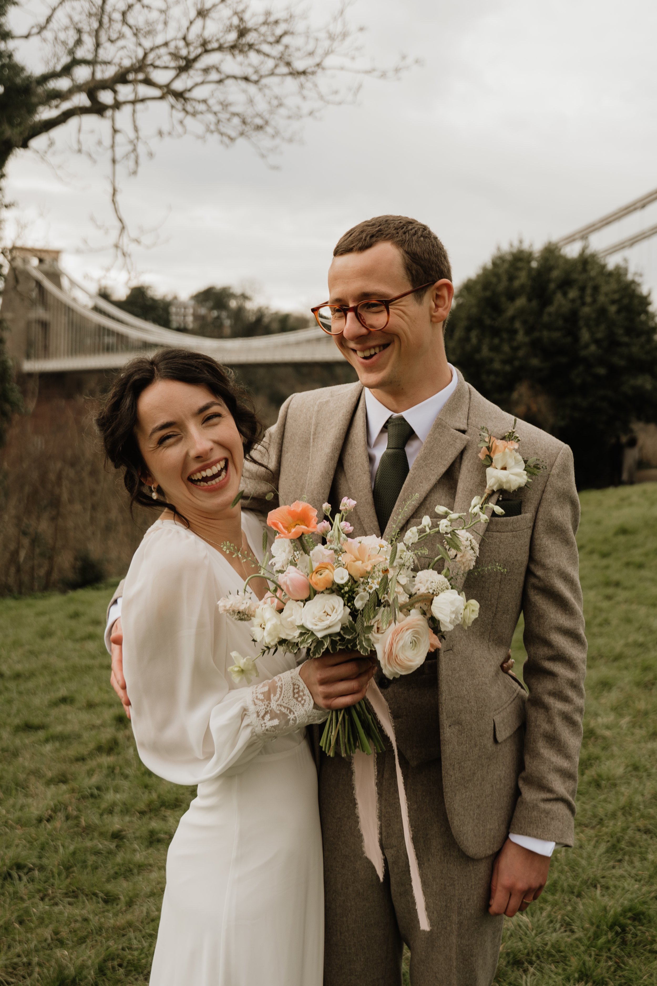 bride and groom laughing at the camera in front of the bristol suspension bridge