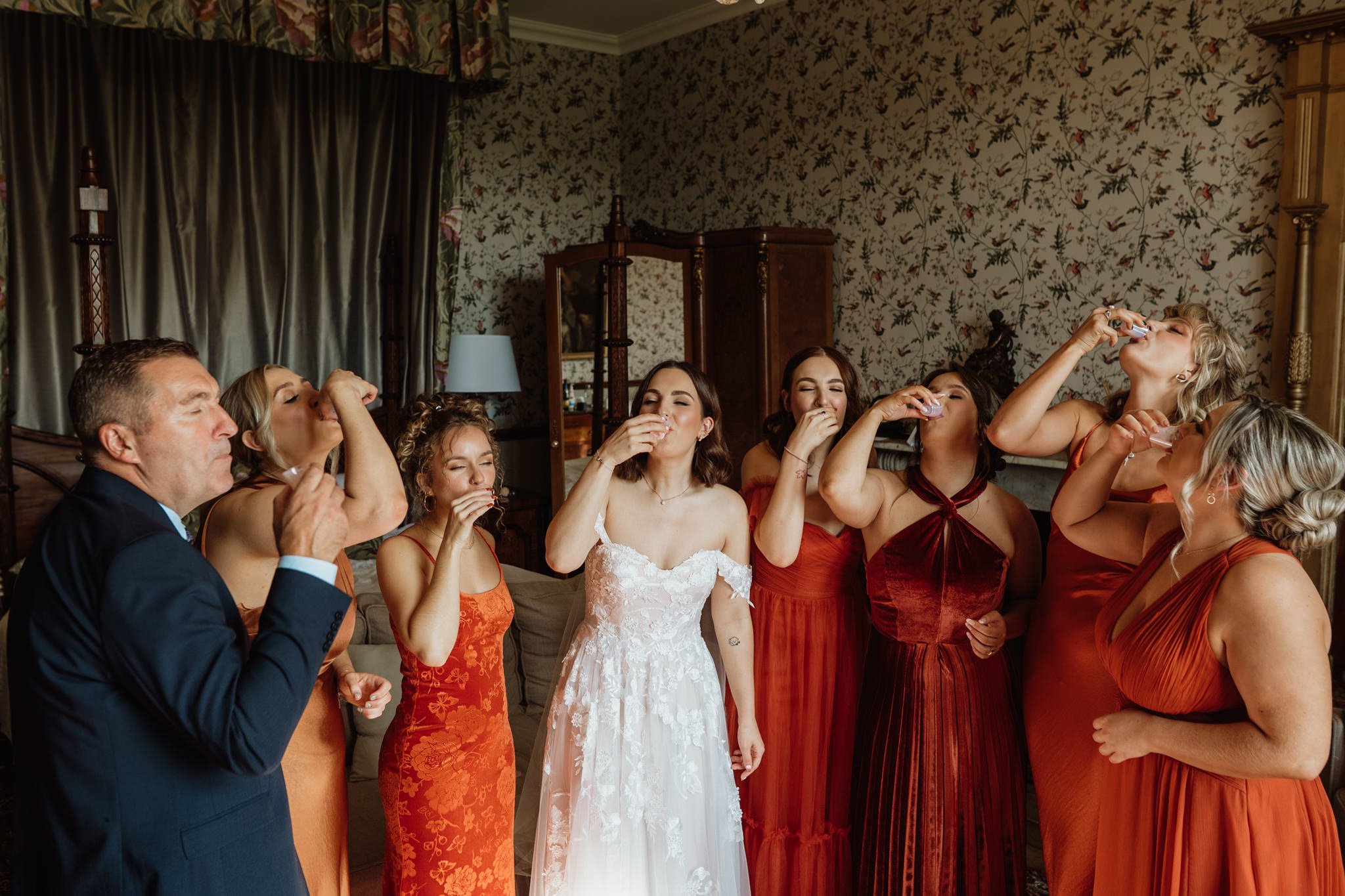 bride and bridesmaids do a shot of tequila in a bedroom