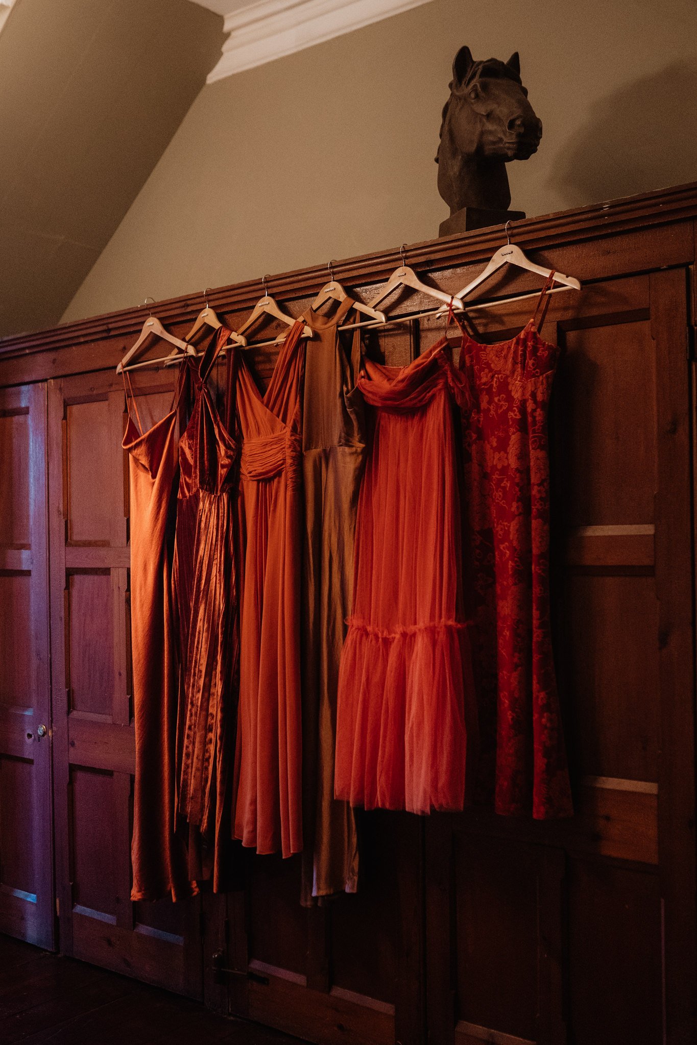 mismatching bridesmaid dresses hanging on wood wall