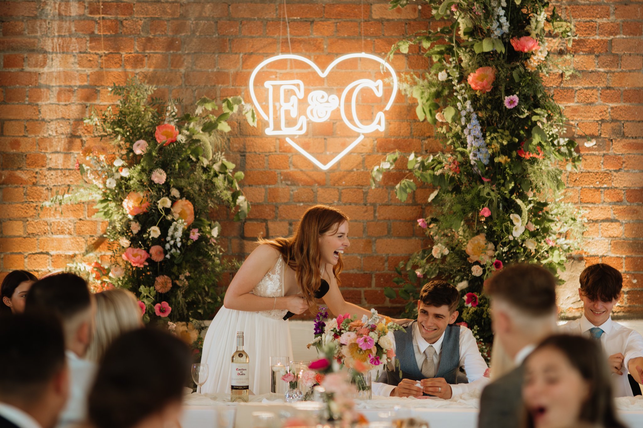 bride laughing during her speach under neon sign of their initials