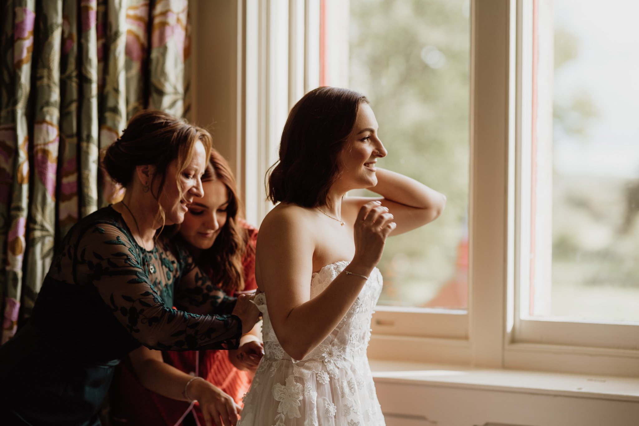 bride's mum and sister doing up the wedding dress