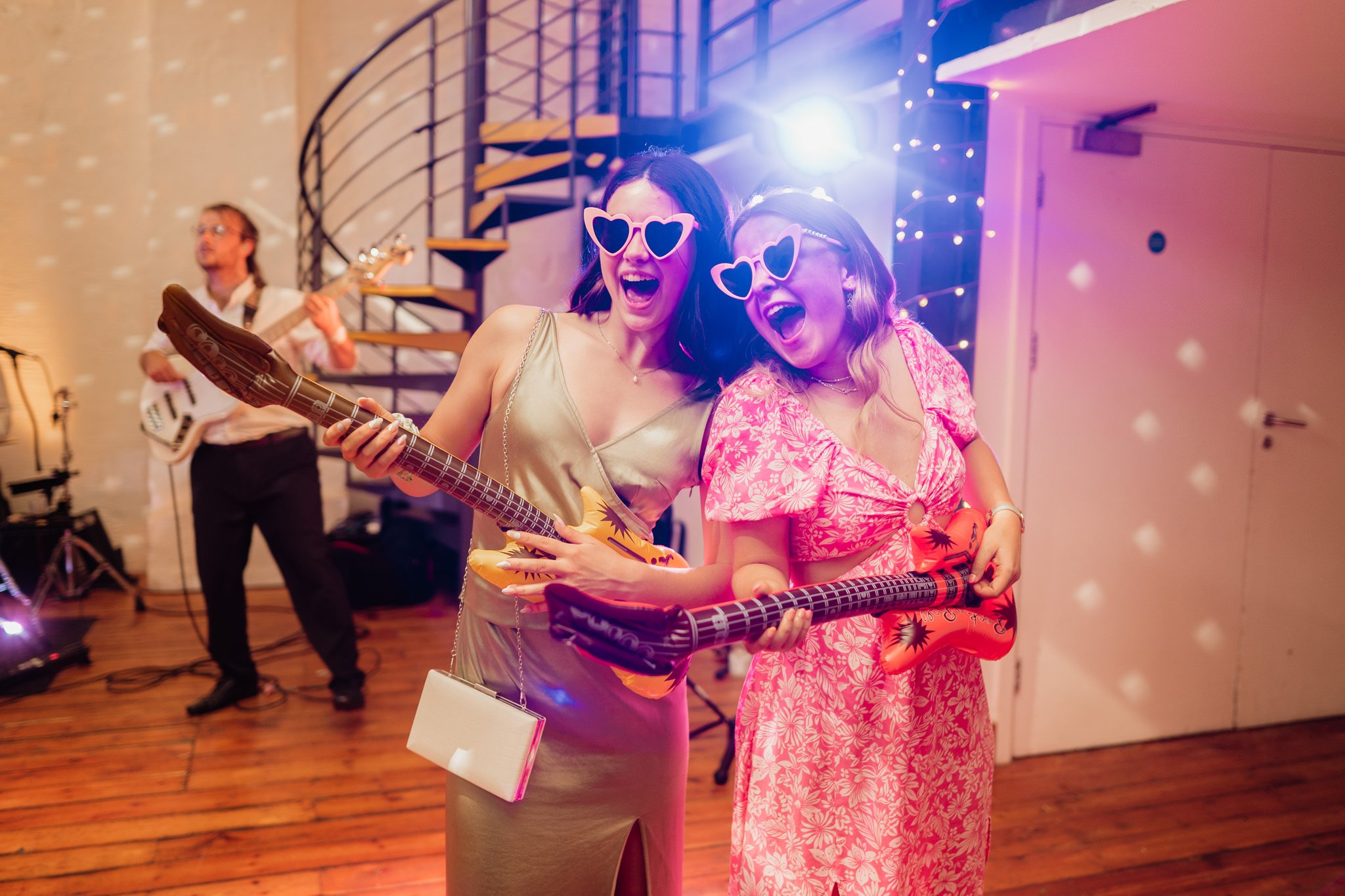 two guests wearing heart shaped sunglasses dancing with inflatable guitars