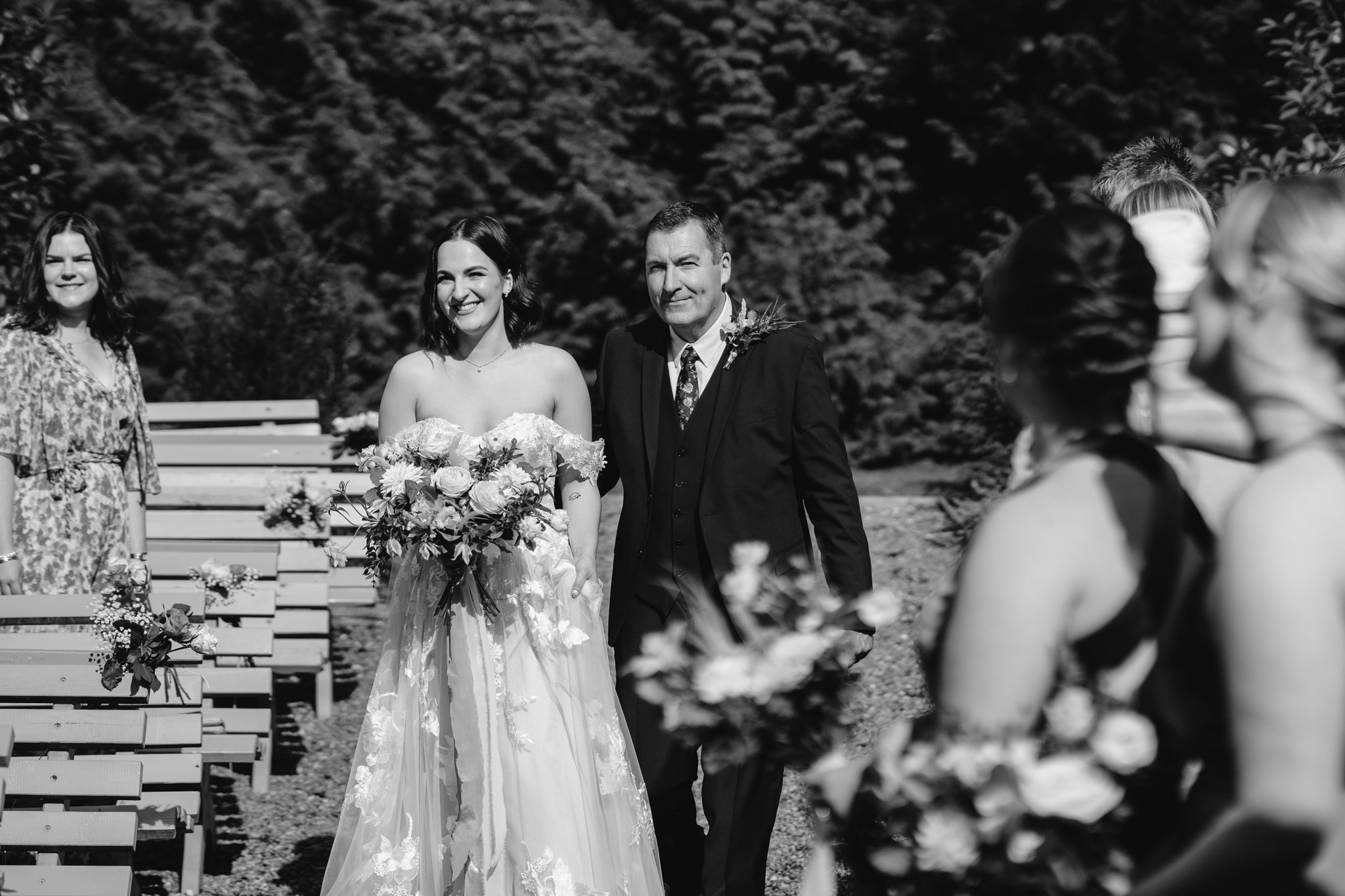 bride walking down aisle outside with dad, black and white