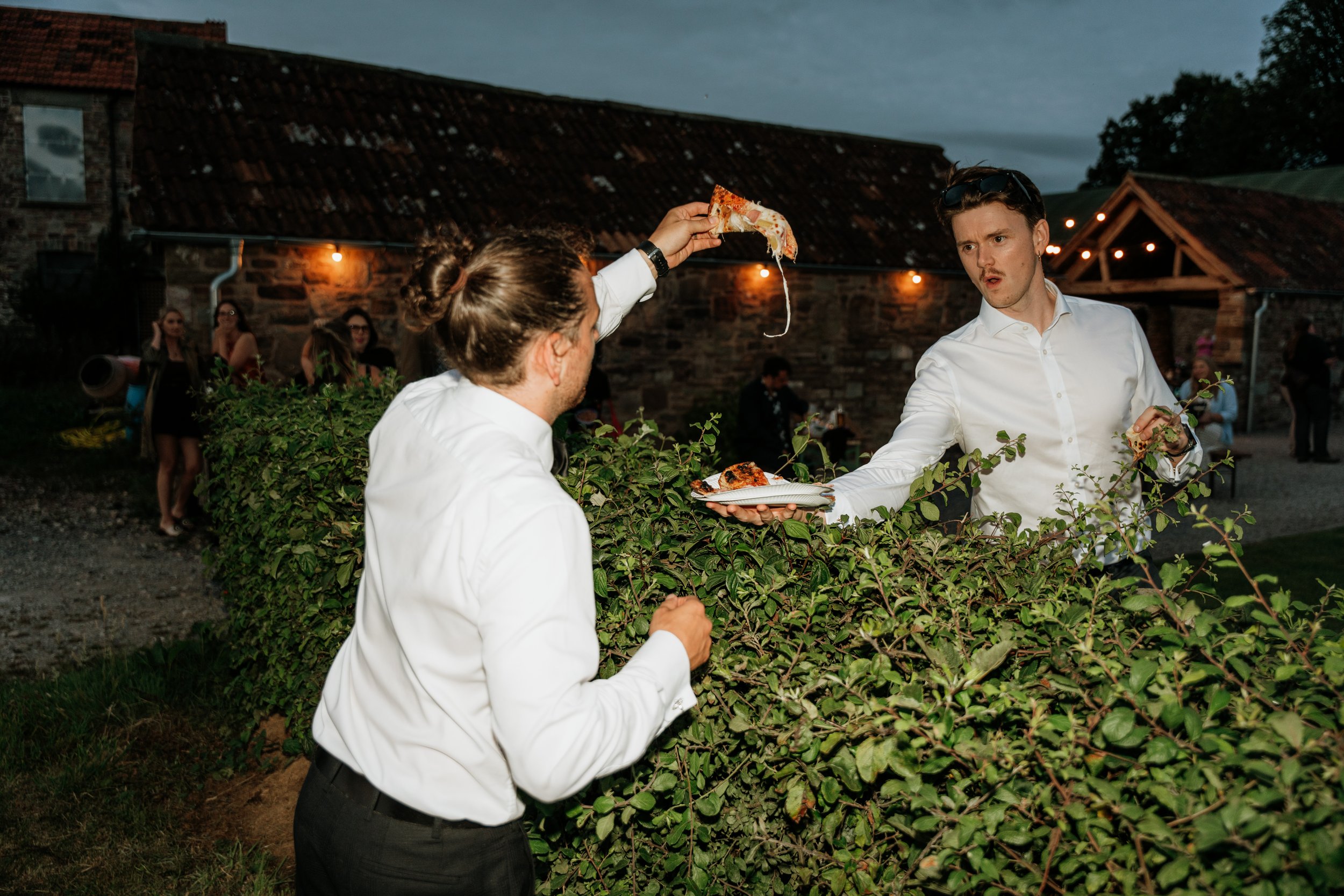 groom grabs a slice of pizza from a guest over a hedge