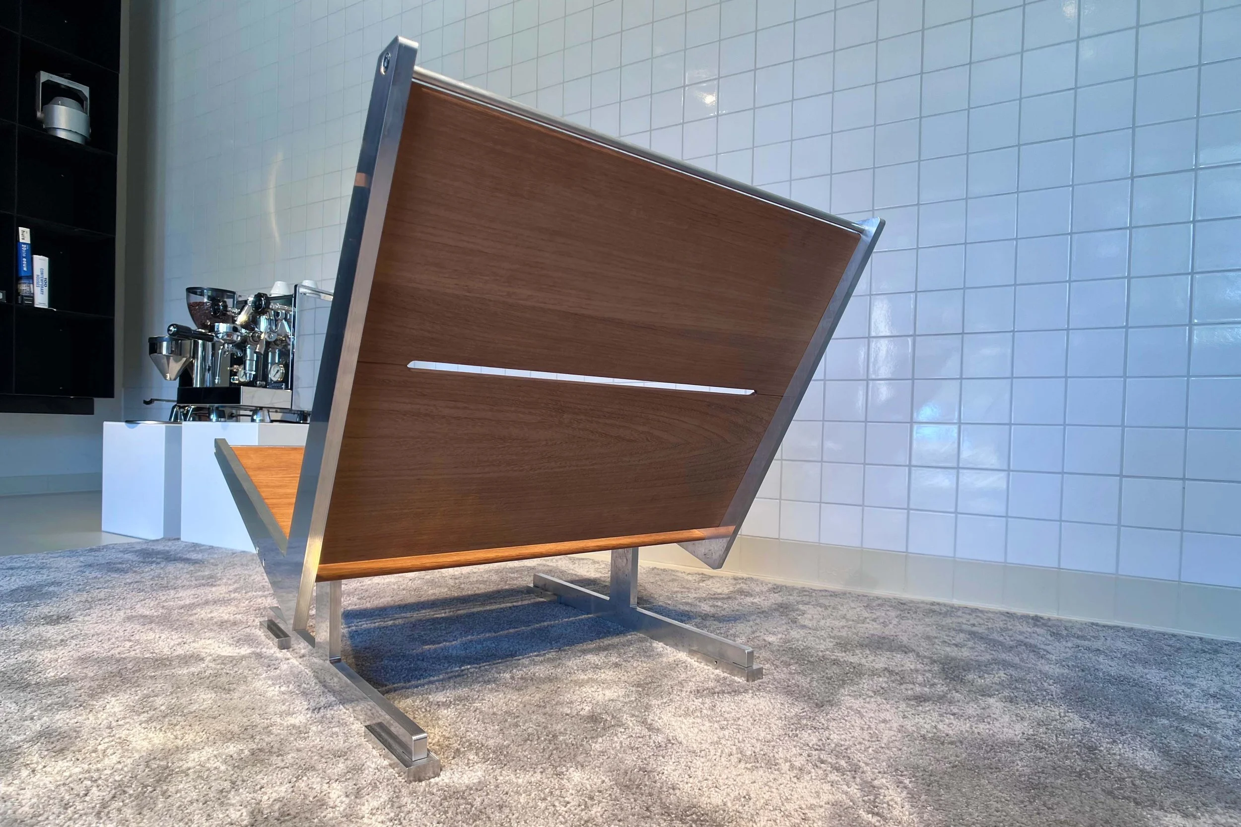 A modern kitchen island with a wood countertop, metal frame, and attached kitchen faucet, set on a plush gray carpet with white tiled wall in the background.