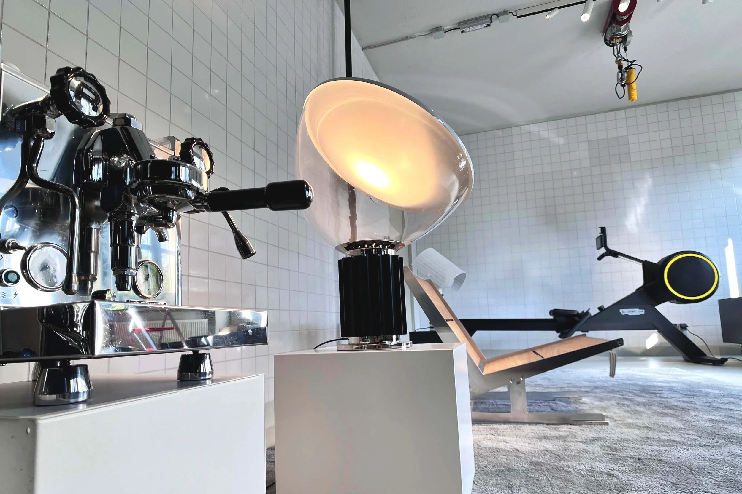 Modern coffee roasting machine with a glowing light in a white-tiled room, with various equipment and tools visible in the surroundings.