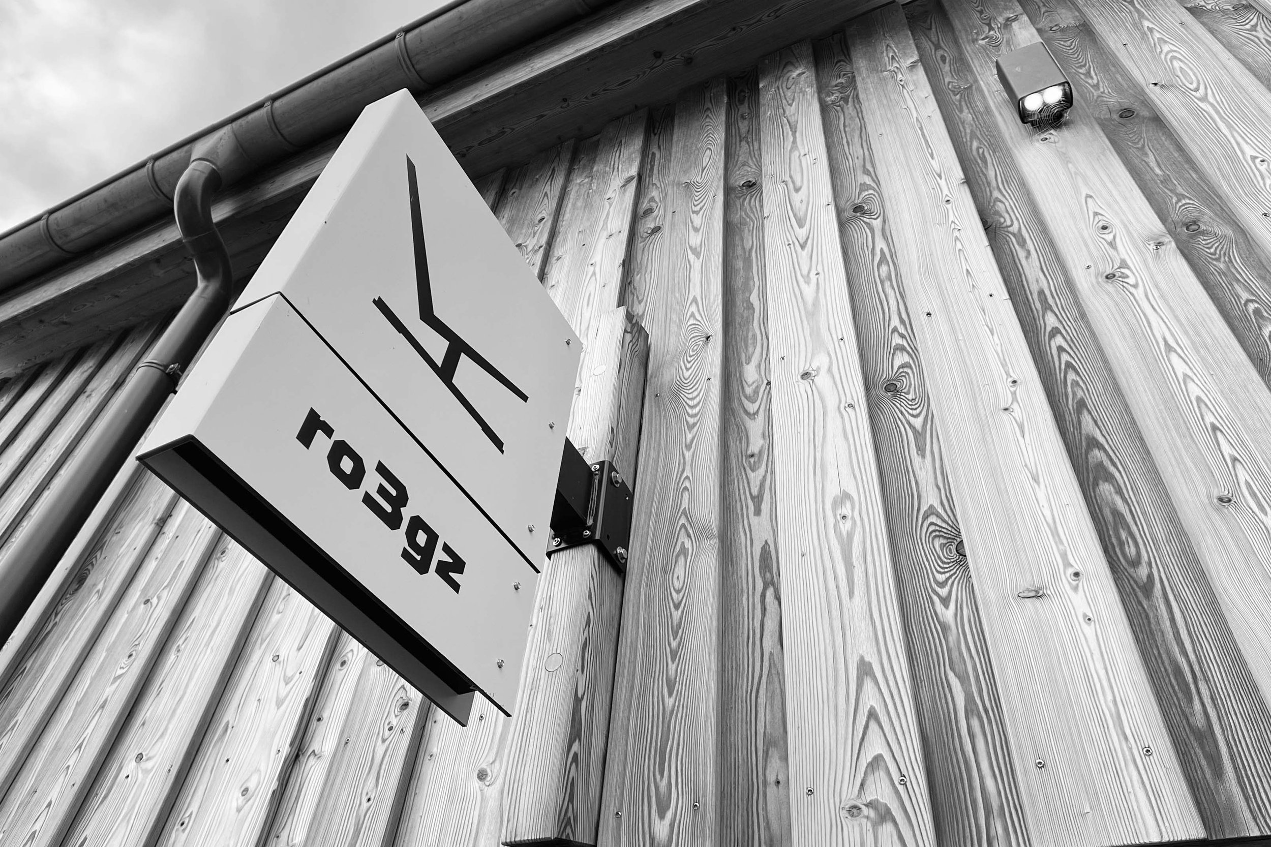 Black and white photo showing an outdoor wooden building wall with a sign that reads 'F.O.B 43' and a security camera mounted above.