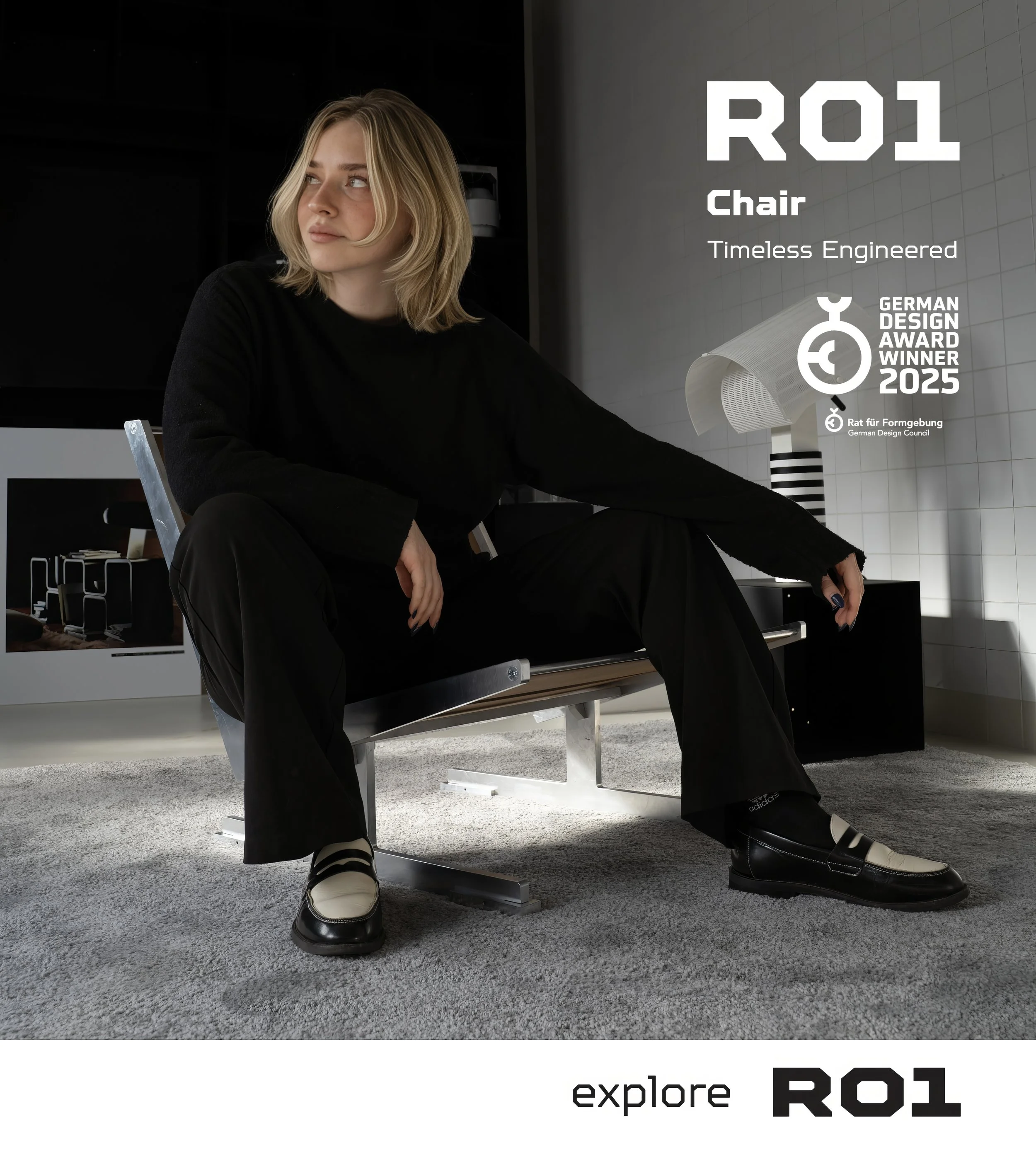 Woman with blonde hair wearing black and white shoes sitting on a bench in a modern interior with a large R01 logo and text that reads 'Chair, Timeless Engineered, German Design Award Winner 2025'.